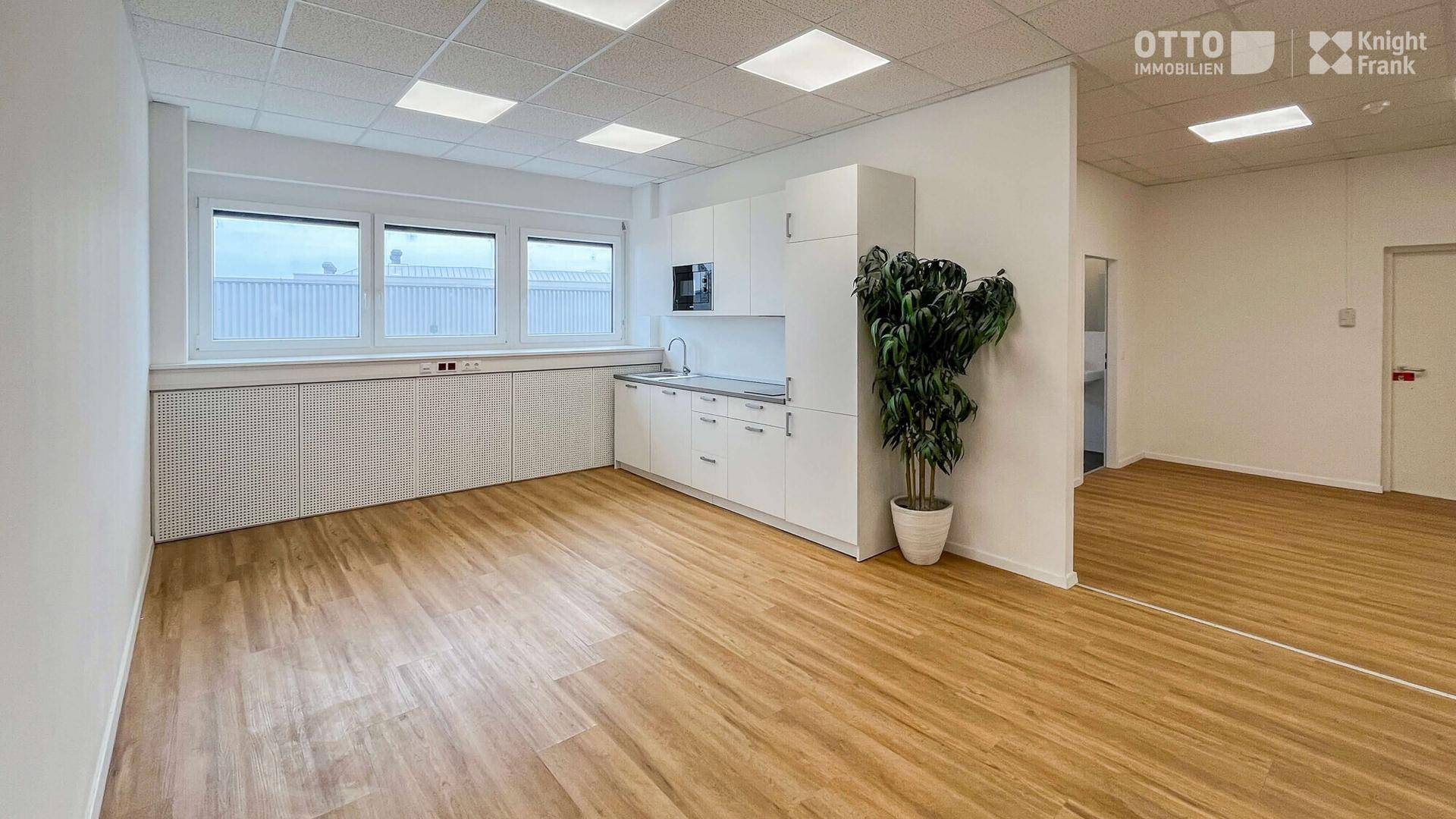 Helles Büro mit integrierter Küchenzeile, großen Fenstern und modernem Laminatboden, in gutem Zustand.