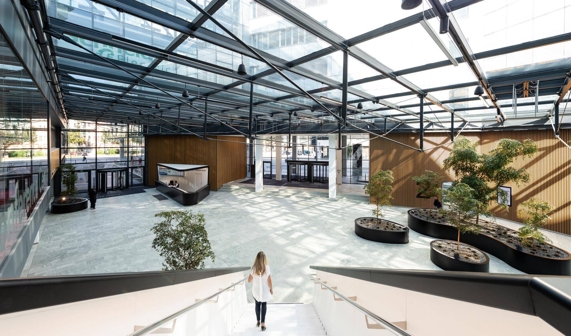 Geräumige, moderne Lobby mit Glasdach, viel Tageslicht und dekorativen Pflanzen in großen Pflanzgefäßen.