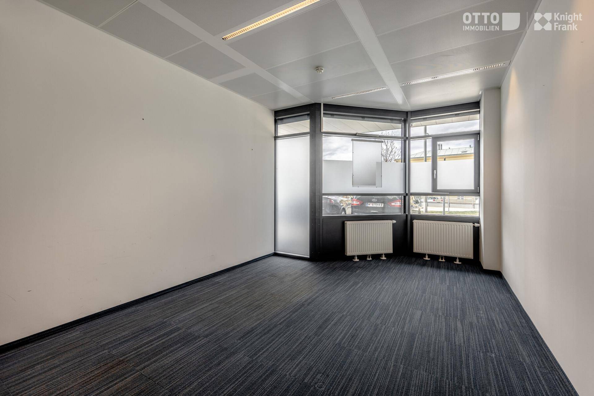 Eckbüro mit großen Fenstern, Teppichboden und weiß gestrichenen Wänden, das viel natürliches Licht bietet.