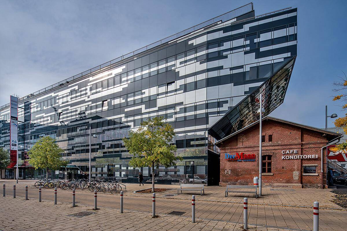 Moderne Bürogebäude-Fassade mit Glas- und Metallstrukturen neben einem traditionellen Backsteingebäude unter blauem Himmel.
