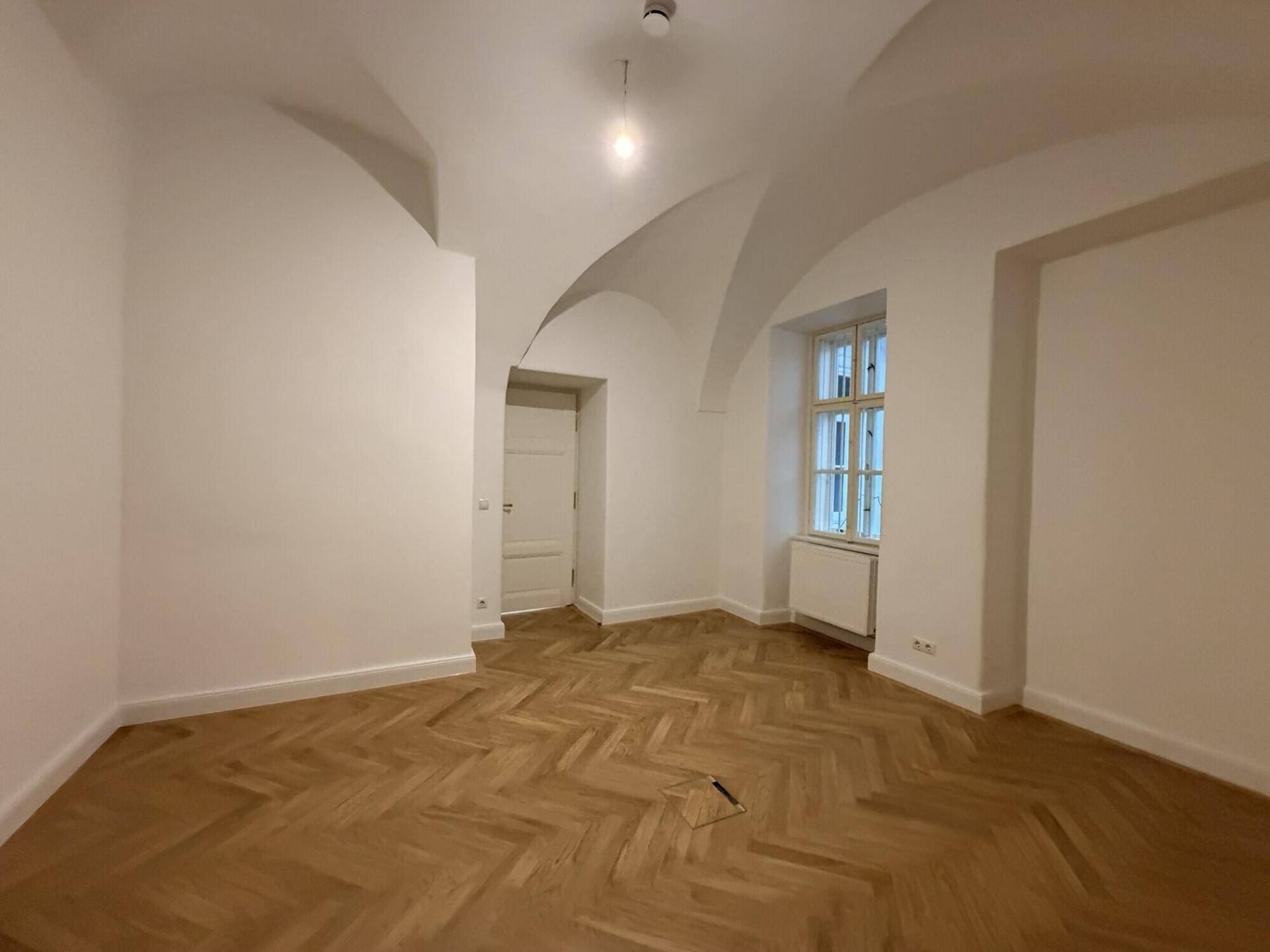 Einzigartiger Raum mit gewölbter Decke, Fischgrätparkett und einem Fenster, das eine besondere Atmosphäre schafft.
