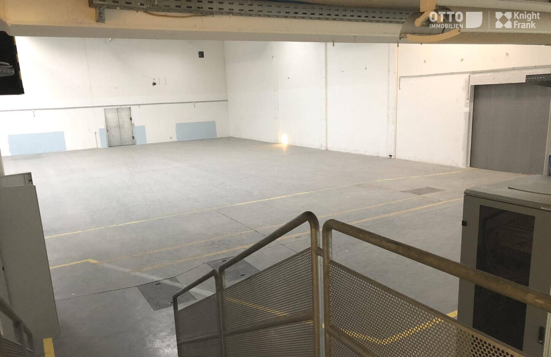Weitläufiger Blick von einer oberen Ebene in die leere Lagerhalle mit Betonboden und hohen Wänden.