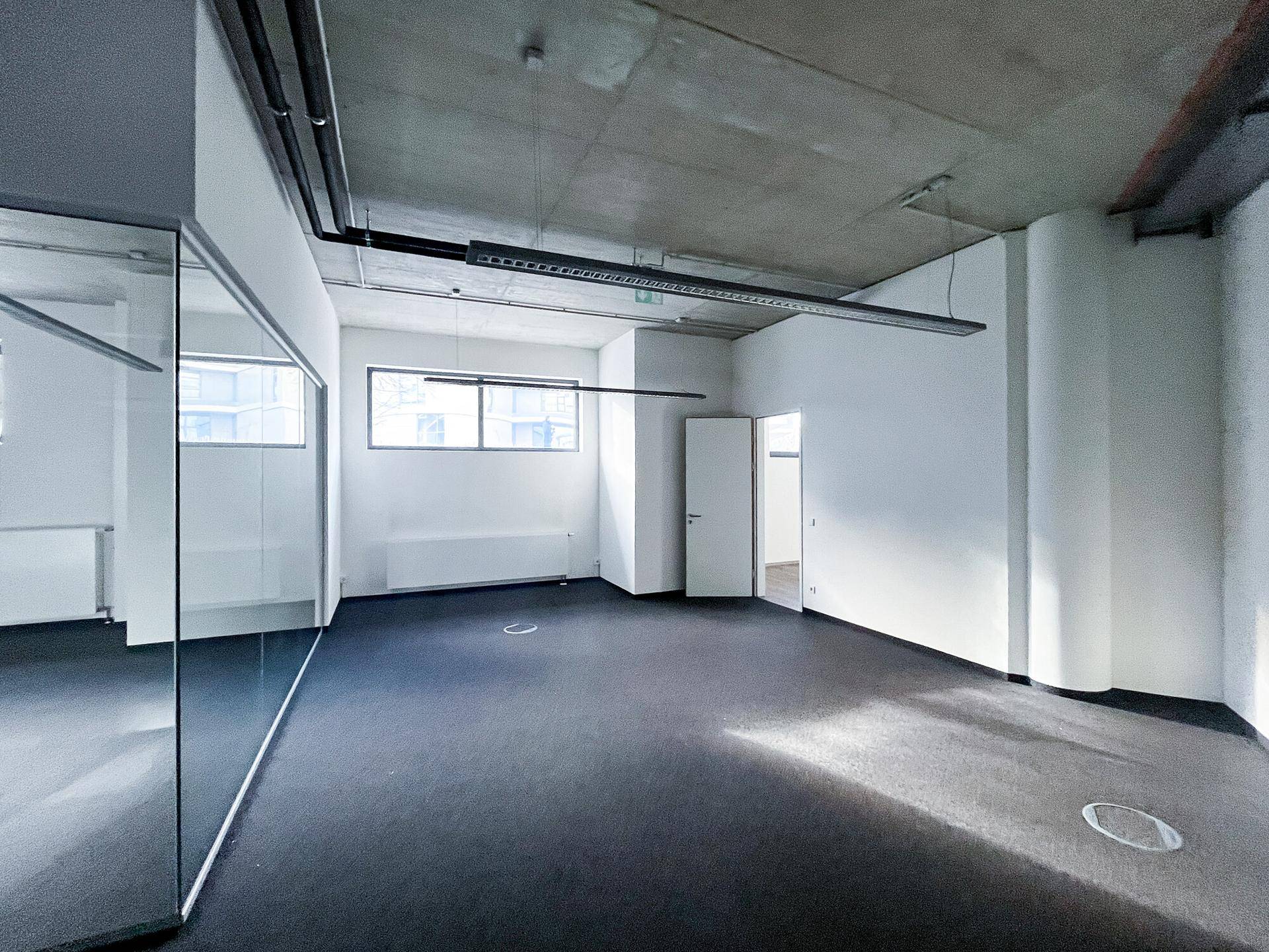 Modernes Büro mit dunklem Teppichboden, großen Fenstern und Glaswänden, bietet viel Tageslicht und offene Atmosphäre.