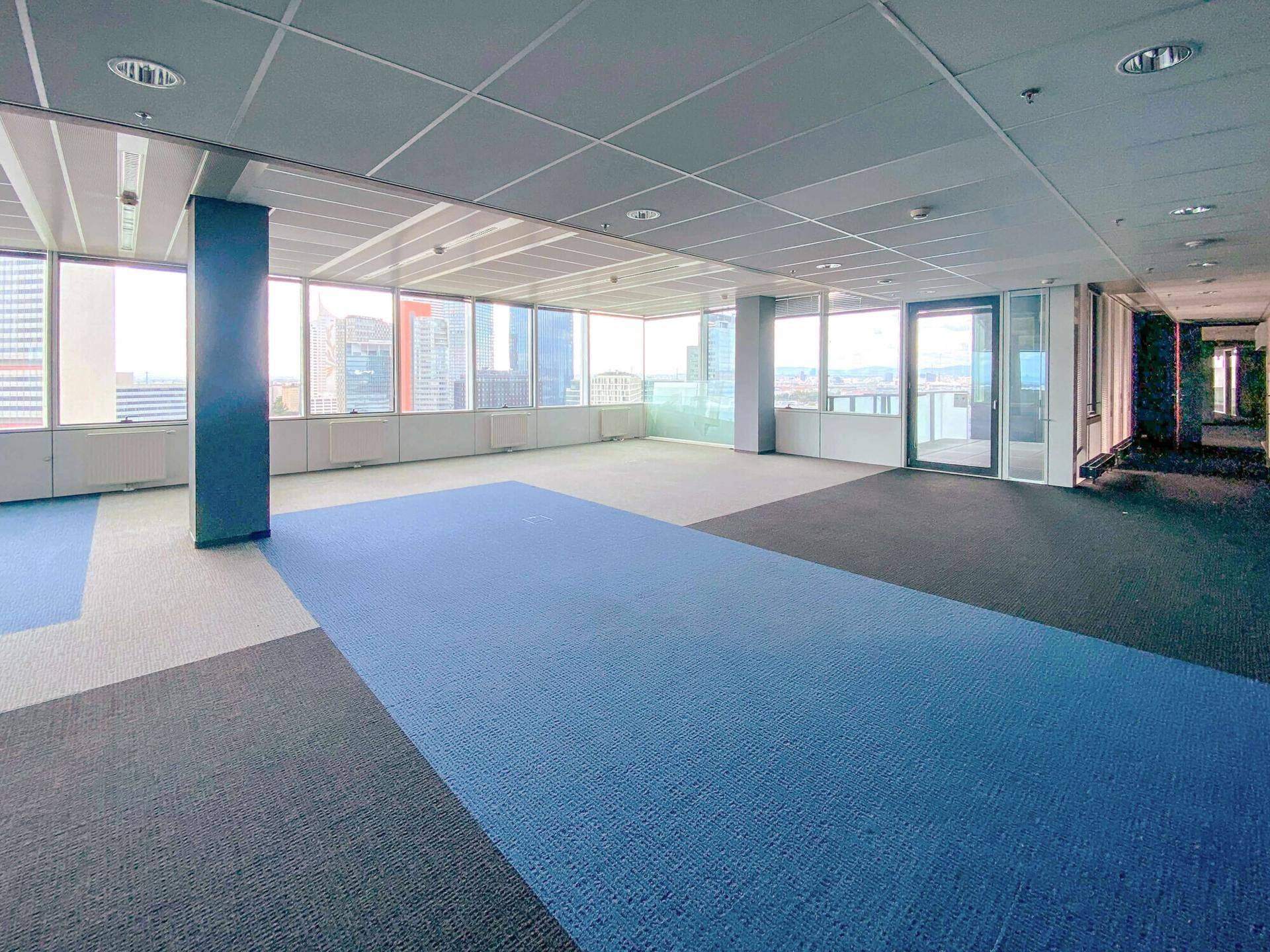 Weitläufiges Büro mit Teppichboden, Säulen und großen Fenstern mit Stadtblick.