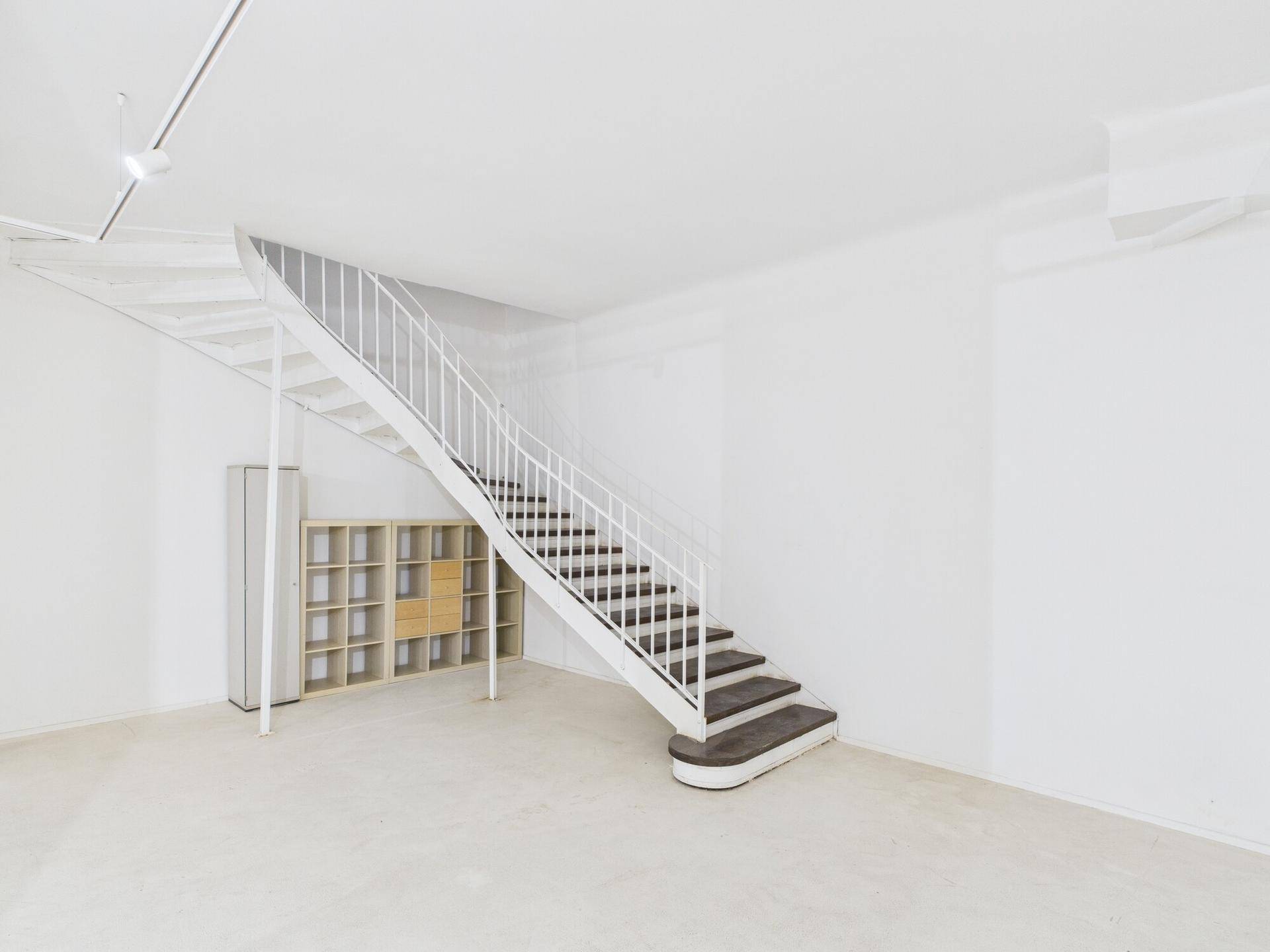 Heller Gewerberaum mit einer eleganten, geschwungenen Treppe und einfachen Regaleinheiten an der Wand.
