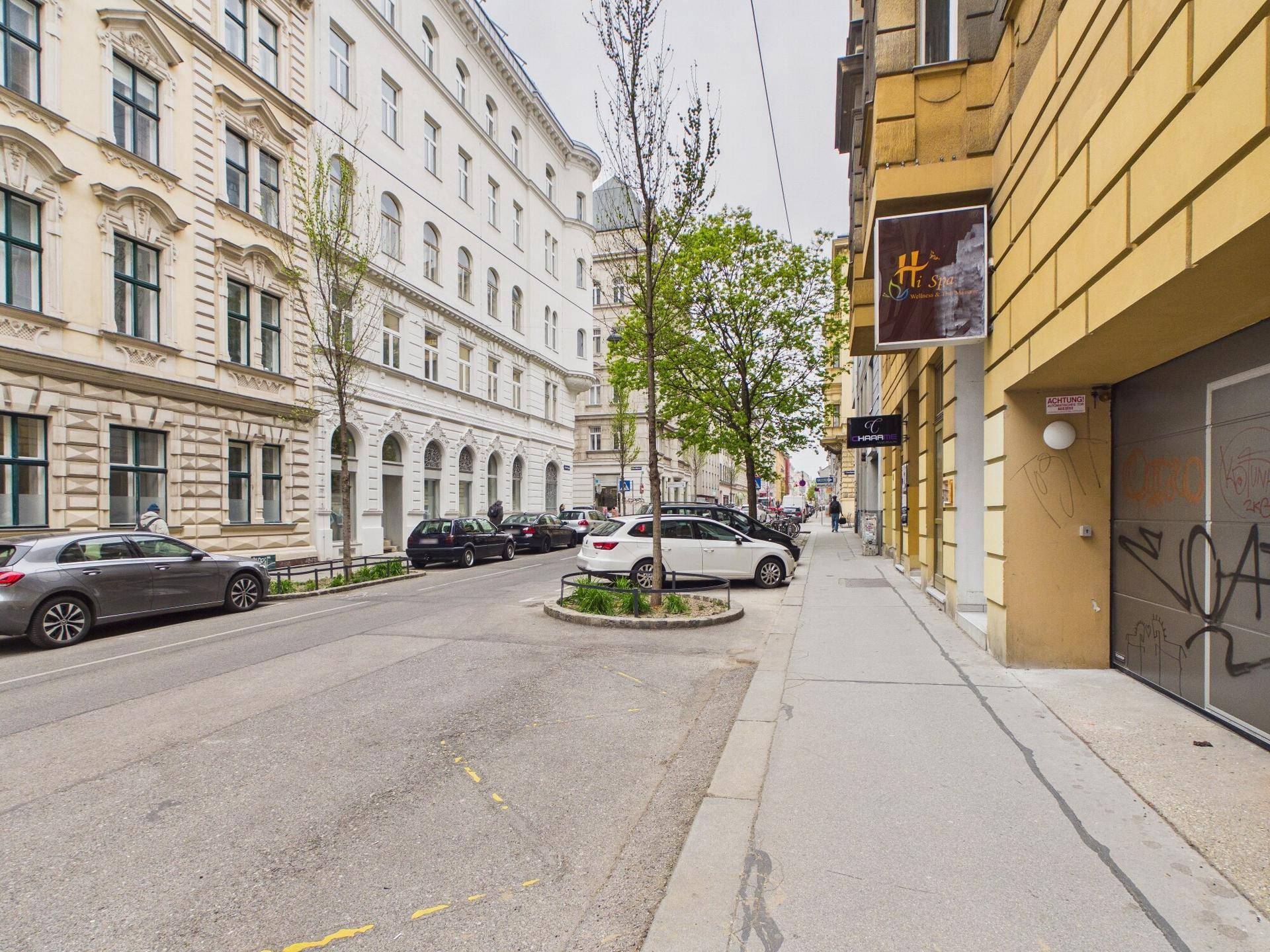 Eine belebte Stadtstraße mit parkenden Autos und historischen Gebäuden in einer urbanen Umgebung.