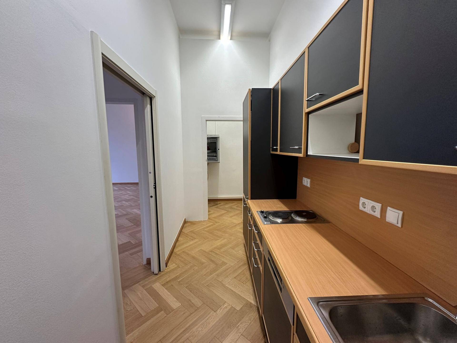 Schmale Teeküche mit dunklen Oberschränken, Holz-Arbeitsplatte und integriertem Kochfeld.