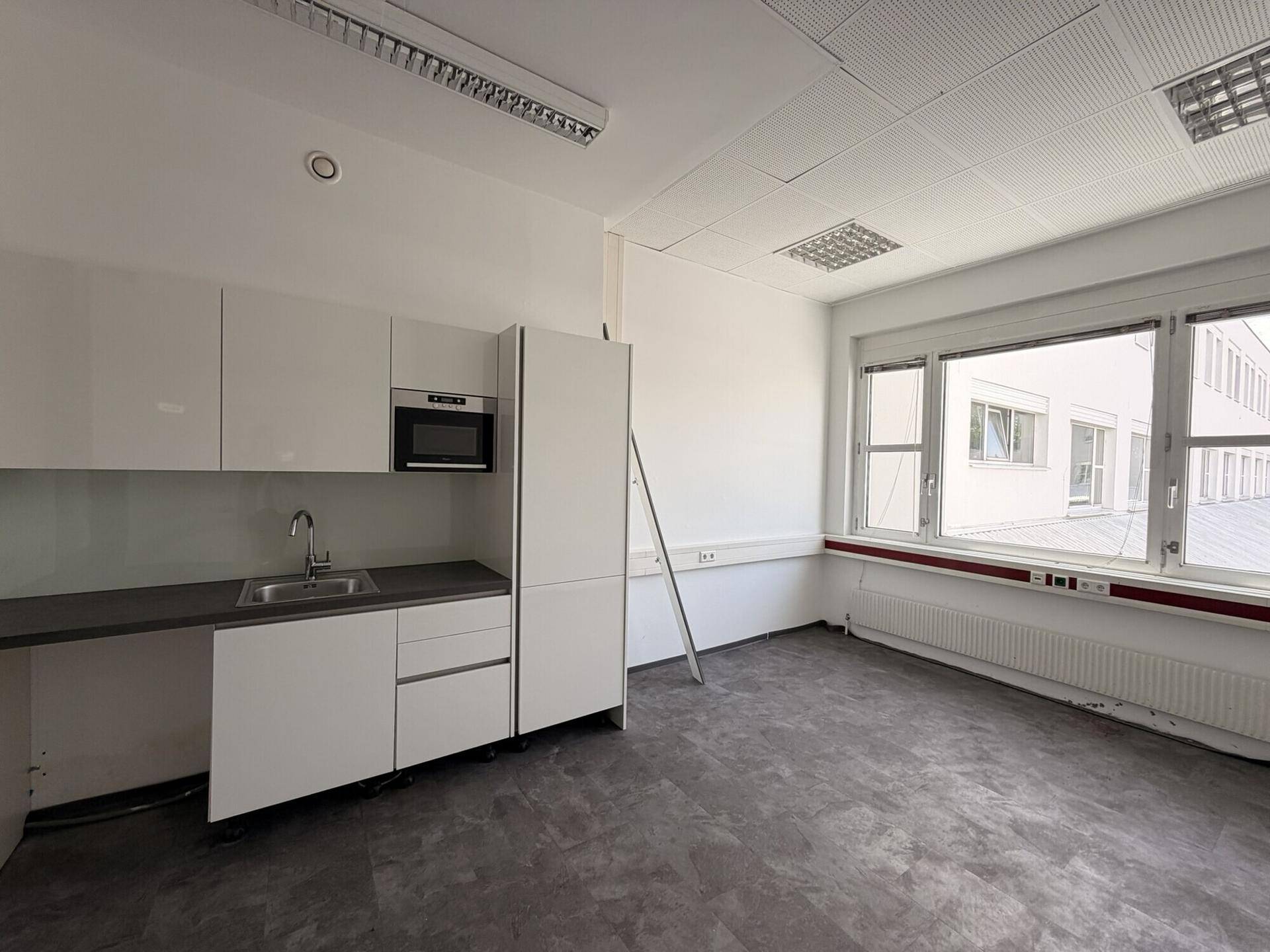 Moderne Küchenzeile mit weißen Hochglanzschränken, Spüle, Mikrowelle und dunkler Arbeitsplatte in einem hellen Raum.