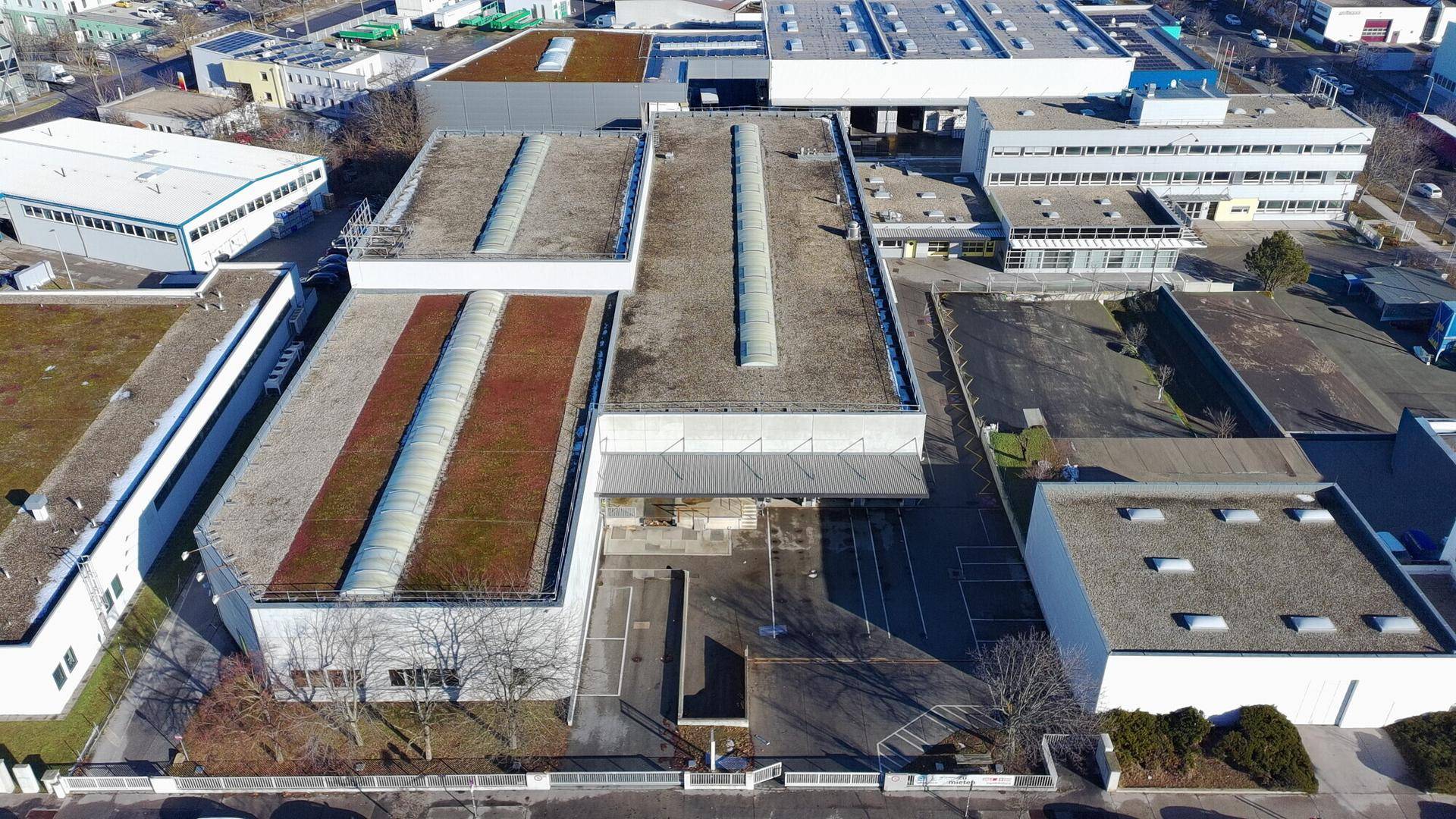Luftaufnahme eines Gewerbegebiets mit mehreren Gebäuden, Flachdächern, einigen Gründächern und Parkplätzen.