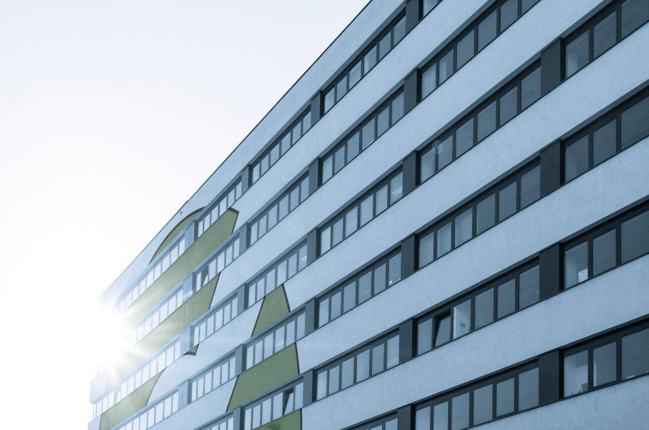 Nahaufnahme der Gebäudefassade mit dynamischen Formen und der Sonne, die sich in den Fenstern spiegelt.
