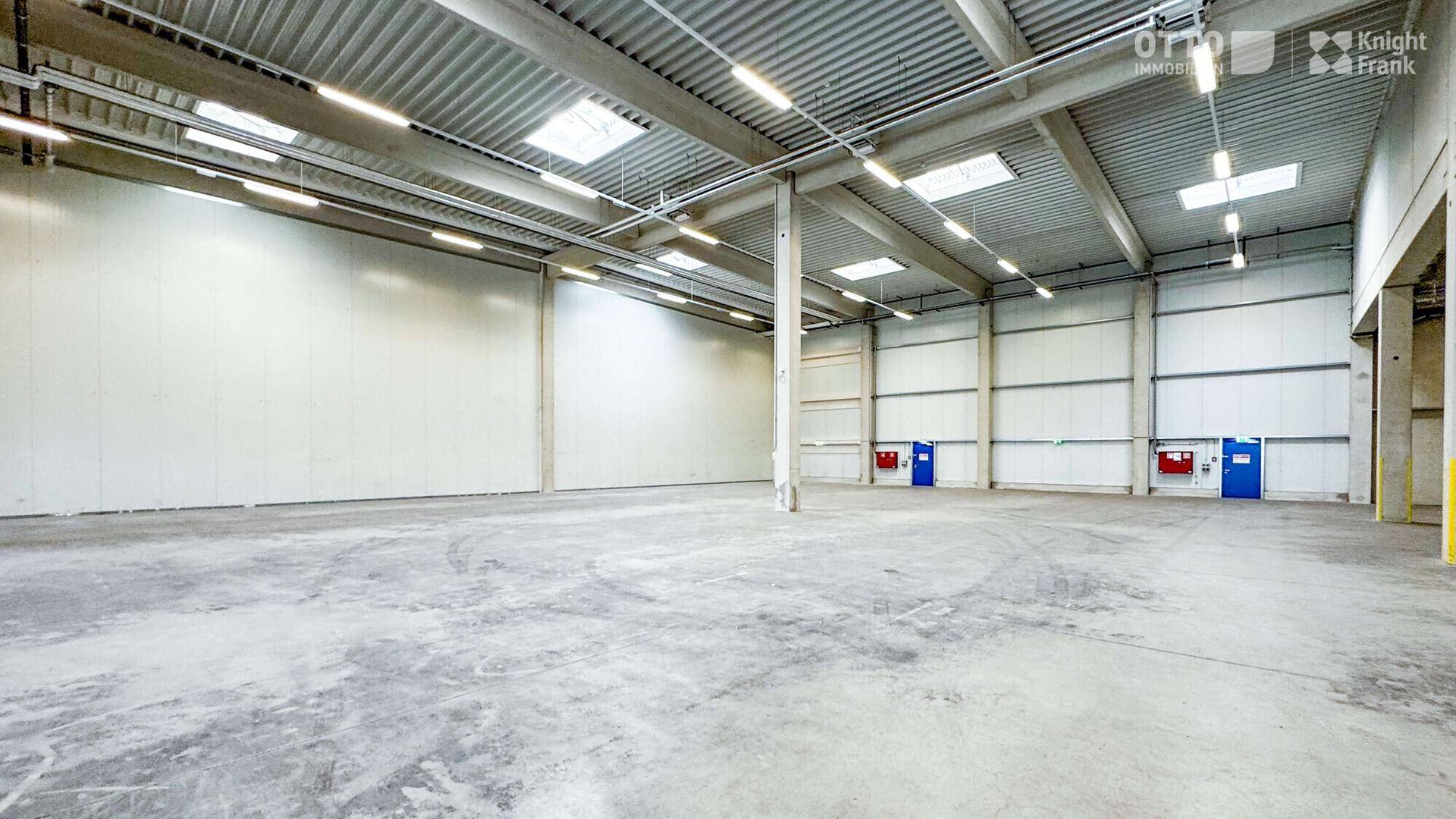 Weitläufige, leere Lagerhalle mit hohen Decken, Oberlichtern und Betonboden, bereit zur Nutzung.