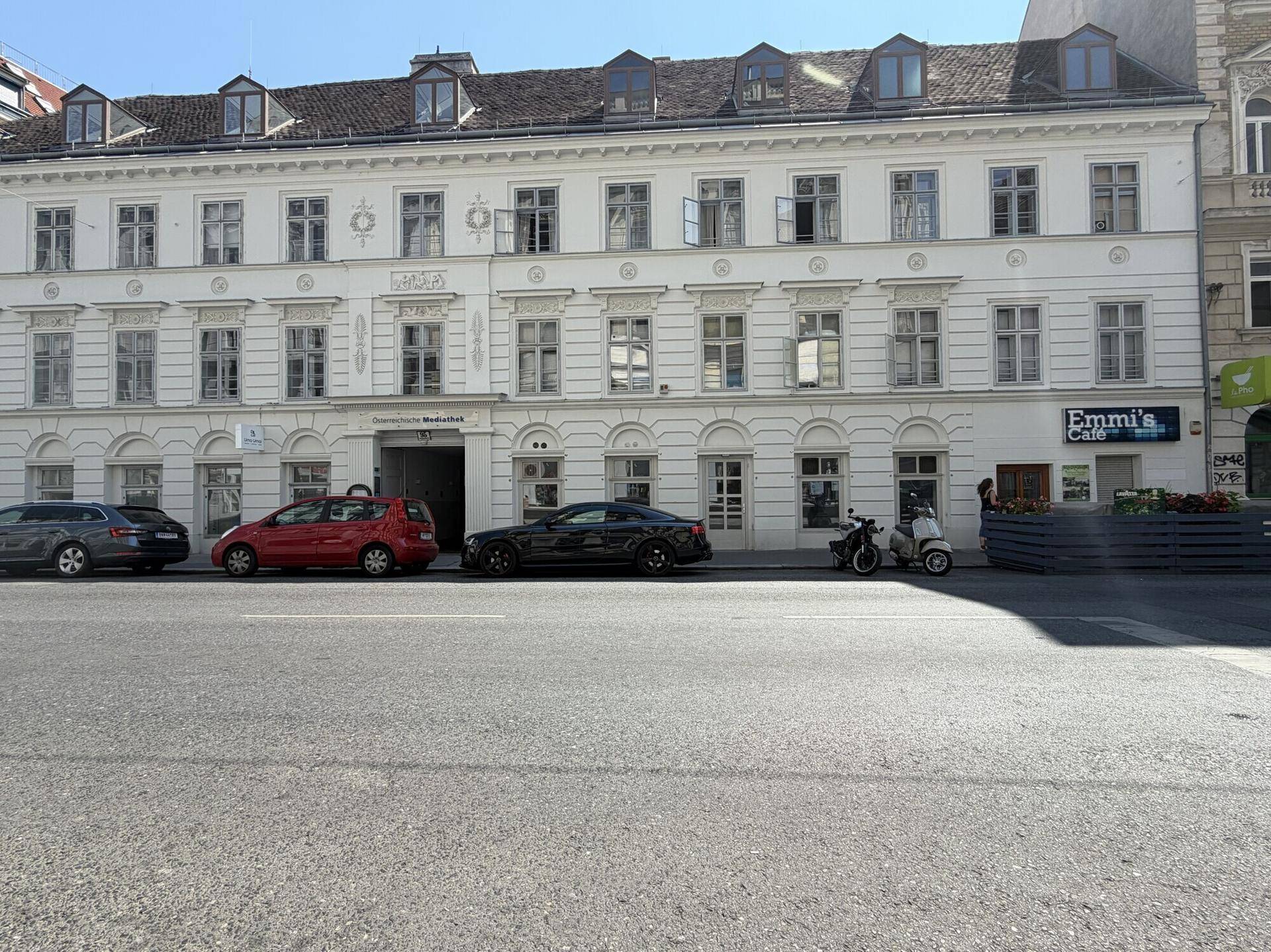 Gesamtansicht eines mehrstöckigen Gebäudes mit klassischer Fassade und geparkten Autos davor.