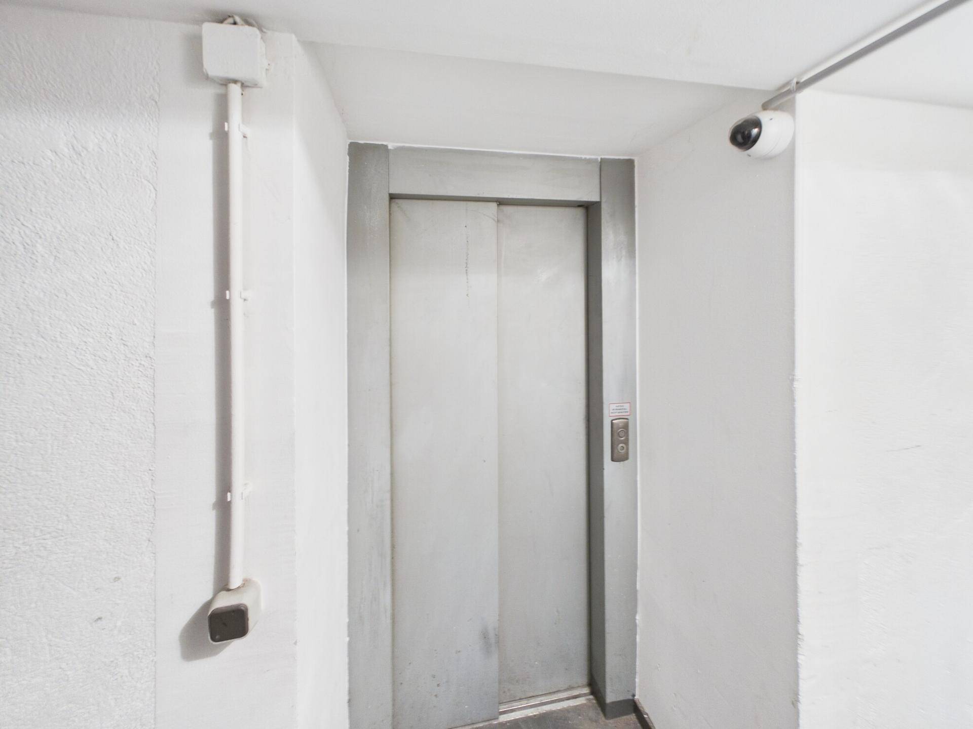 Einfacher Aufzugsbereich mit Metalltüren und einer Überwachungskamera an der Wand.