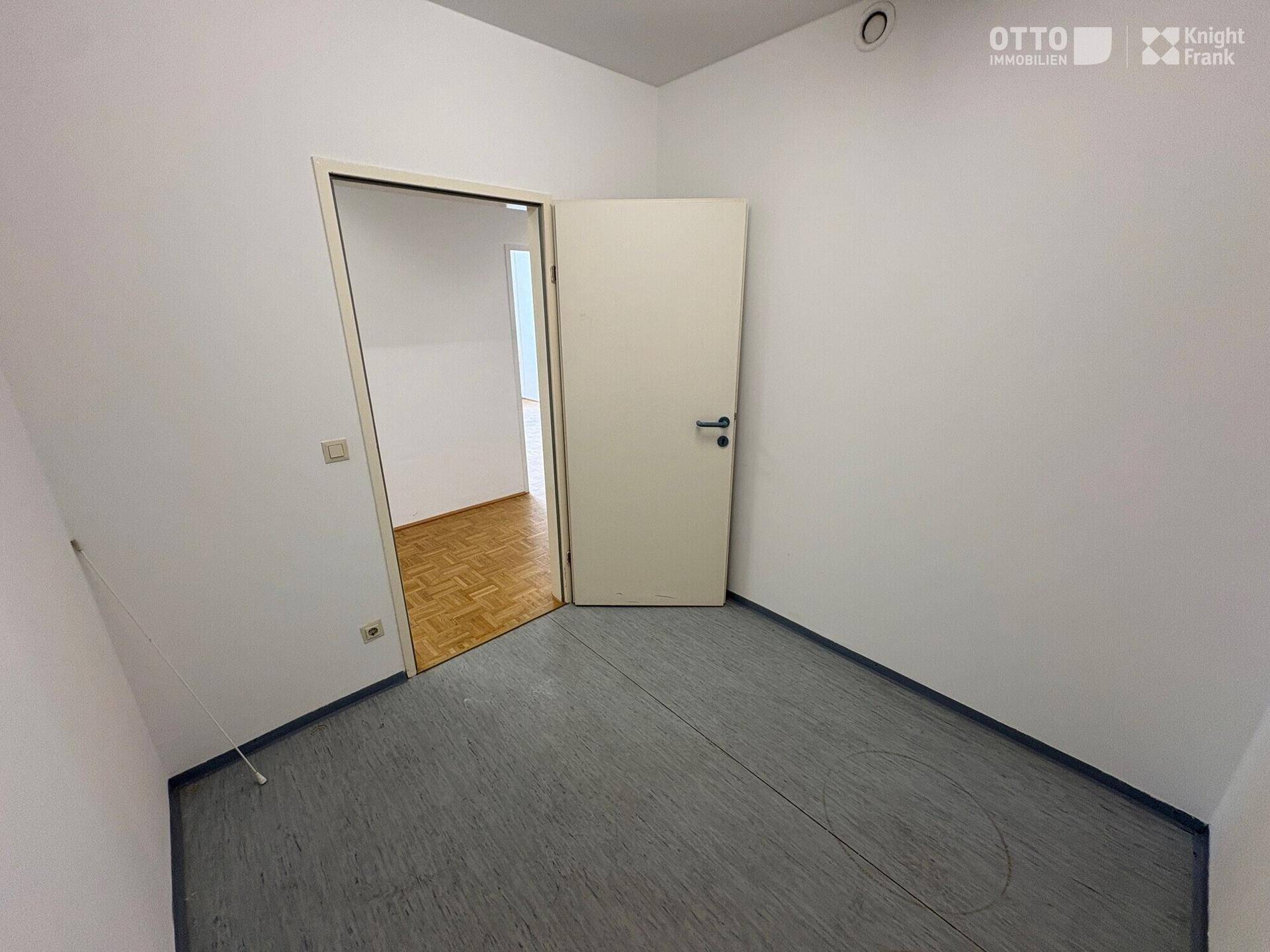 Kleineres Büro mit grauem Vinylboden und weiß gestrichenen Wänden, ideal als Einzelbüro oder Abstellraum.