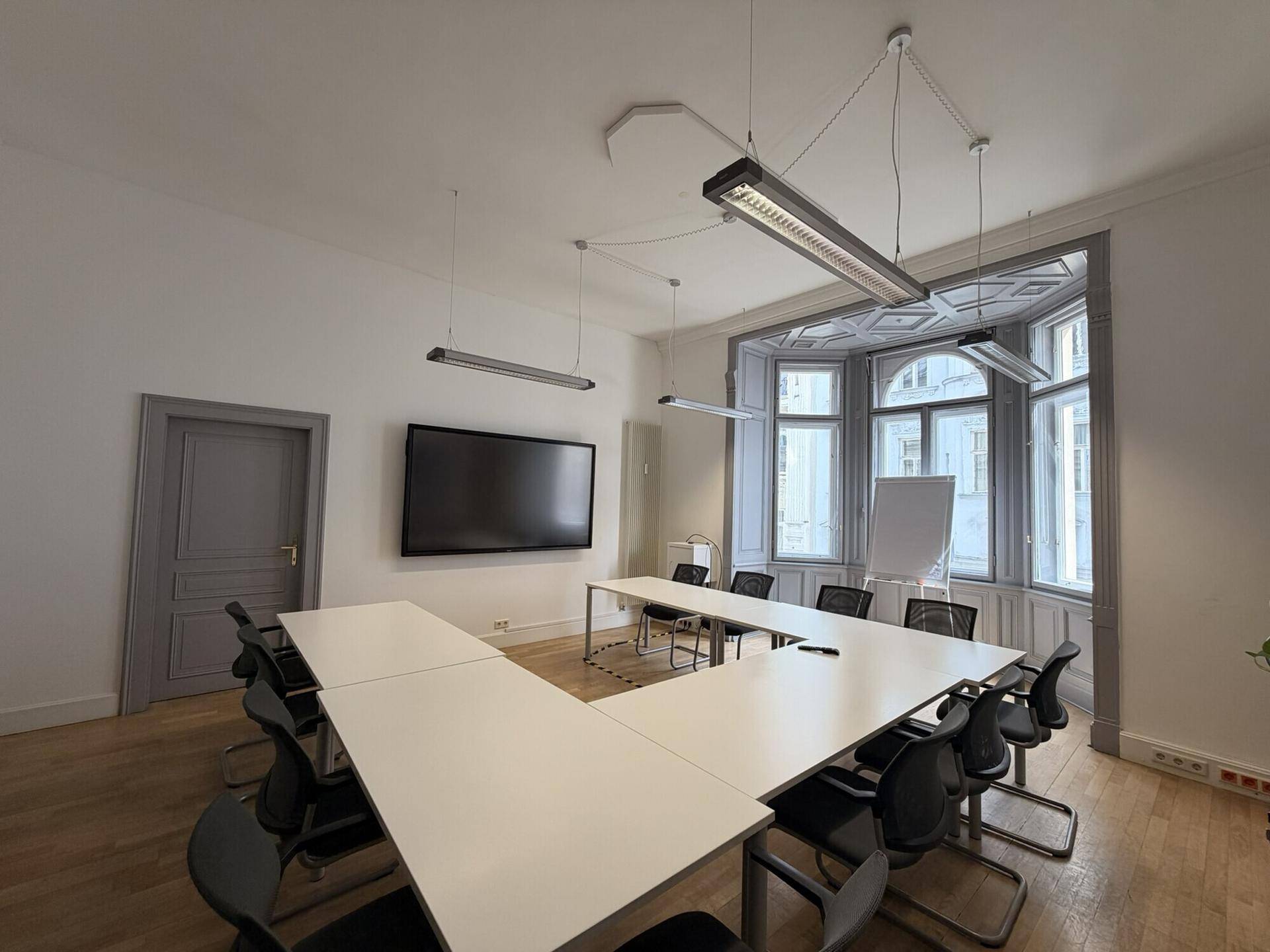 Großer Konferenzraum mit U-förmigem Tisch, Holzboden und einem Erkerfenster mit viel Tageslicht.