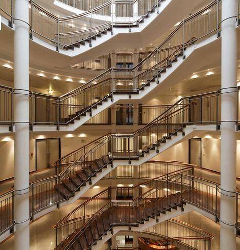 Großes, mehrstöckiges Treppenhaus mit eleganten Geländern und Säulen in einem modernen Gebäude.