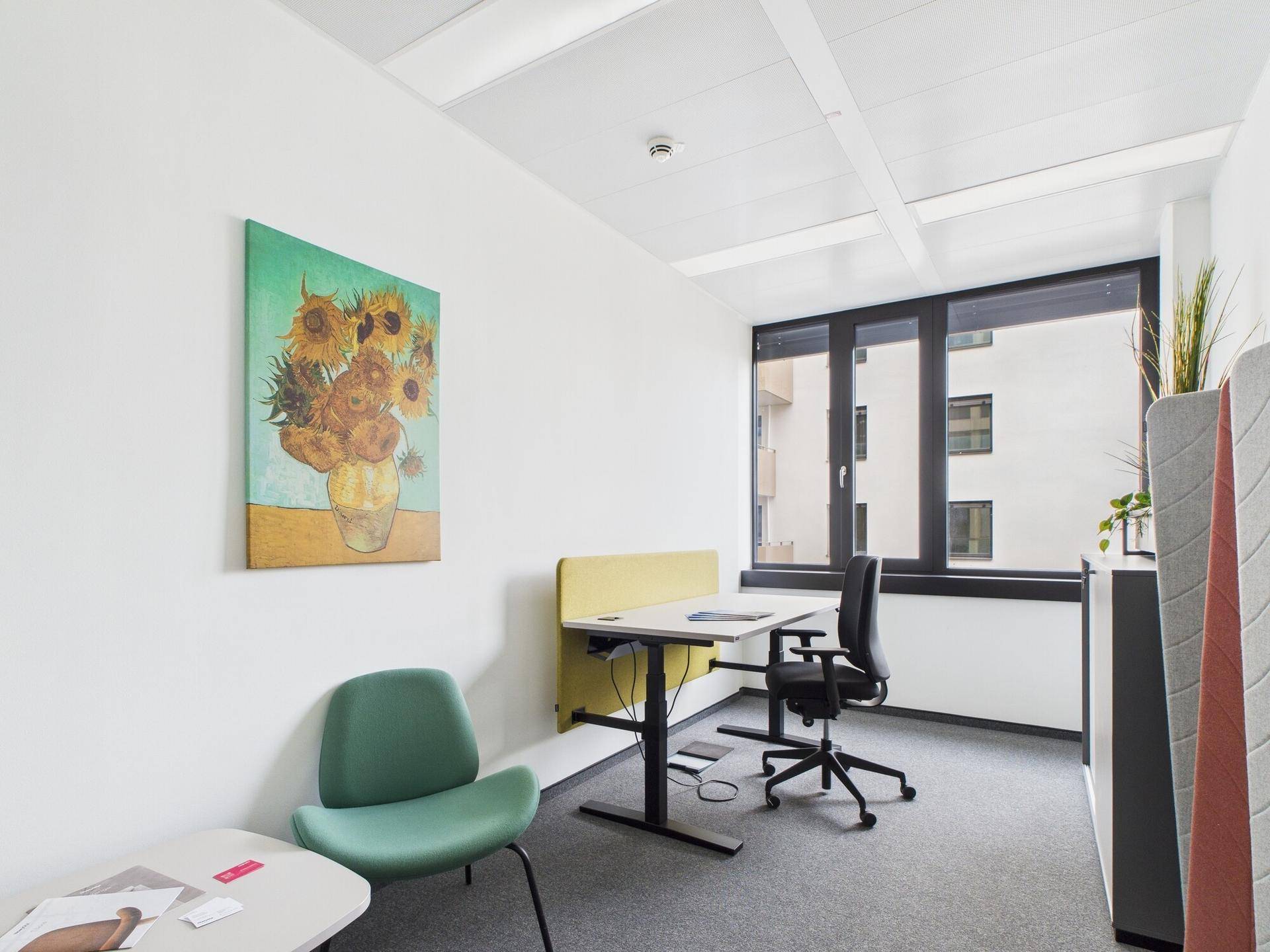 Kleines Büro oder Besprechungszimmer mit Schreibtisch, Stuhl und einem farbenfrohen Kunstwerk an der Wand.
