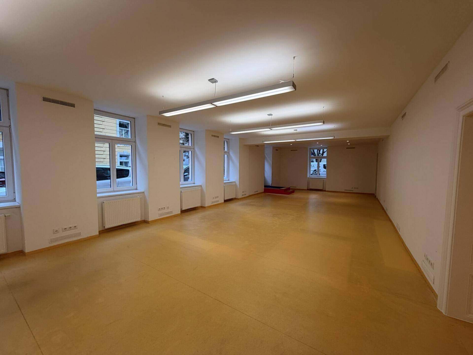 Weitläufiger, leerer Raum mit hellen Wänden und Fenstern, ideal für gewerbliche Nutzung oder Büros.
