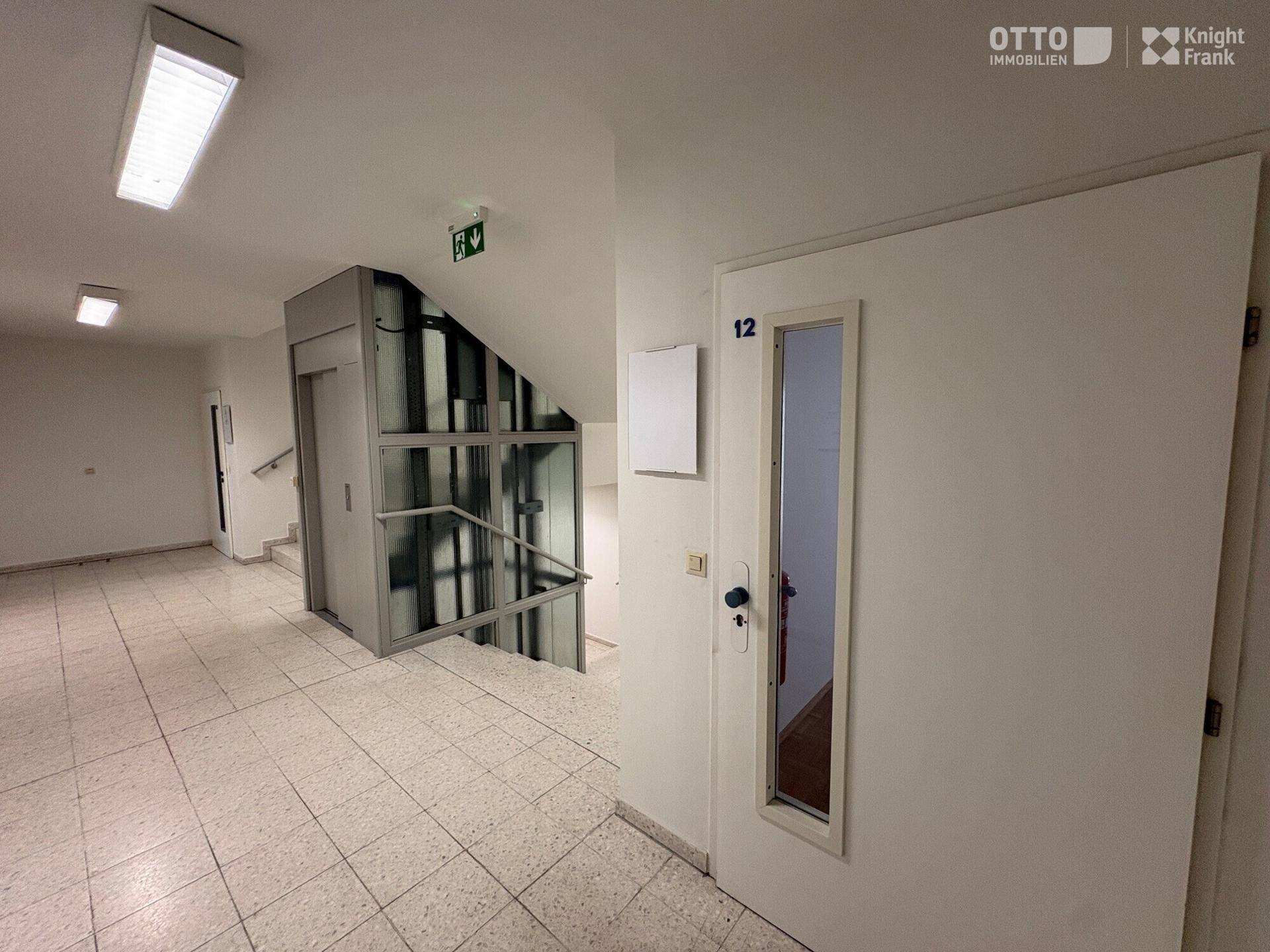 Heller Eingangsbereich mit modernem Aufzug und Treppenhaus, ausgestattet mit Fliesenboden und guter Beleuchtung.