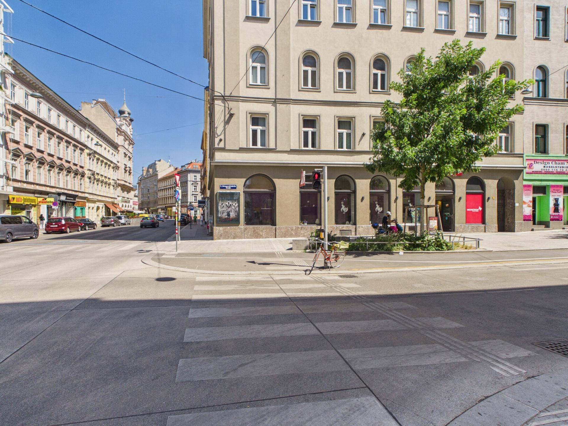 Gebäude an einer Straßenecke mit Geschäften im Erdgeschoss und Wohnungen darüber, umgeben von städtischer Architektur.
