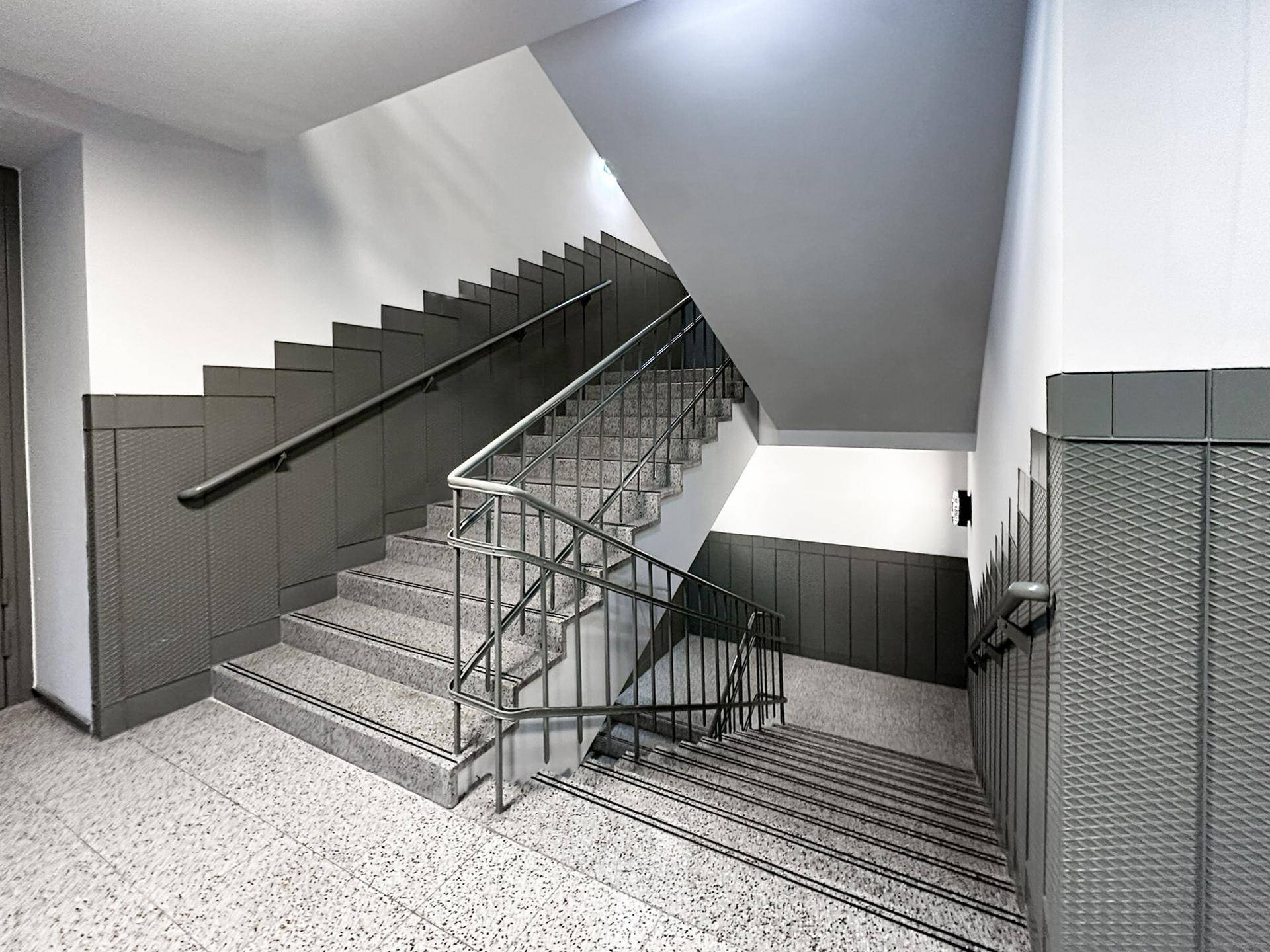 Geräumiges Treppenhaus mit Terrazzoboden und Metallgeländer, das mehrere Stockwerke verbindet.