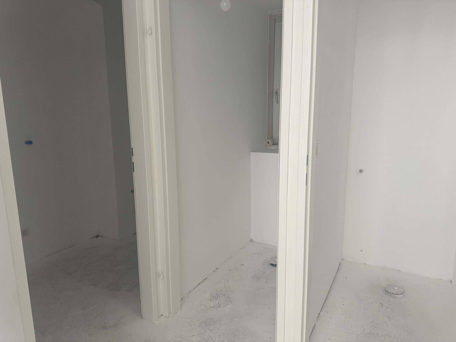 Mehrere kleine, unfertige Räume mit weißen Wänden und Betonböden, möglicherweise für Sanitäranlagen.