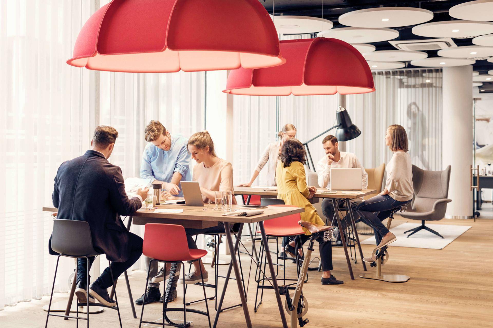 Belebter Co-Working-Bereich mit modernen Möbeln, auffälligen roten Pendelleuchten und Holzboden, ideal für Zusammenarbeit.