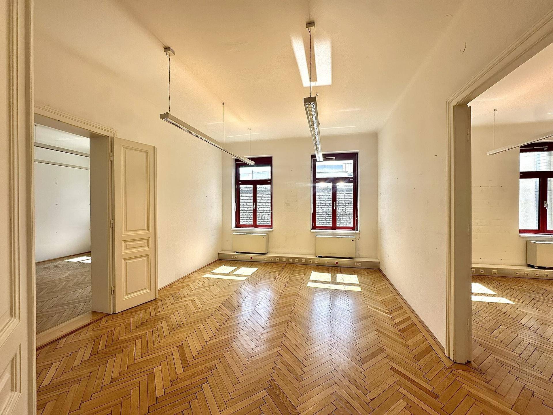 Helles Büro mit klassischem Fischgrätparkett und roten Fensterrahmen, die einen Kontrast bilden.