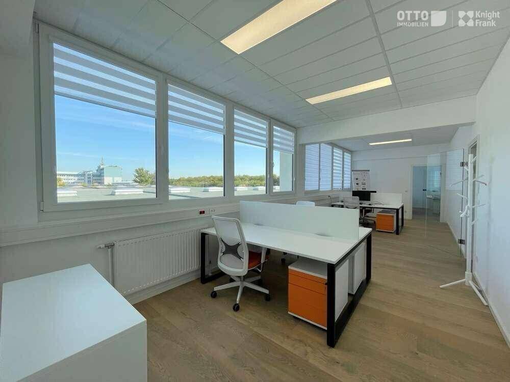 Helles und modernes Büro mit mehreren Arbeitsplätzen, großen Fenstern und Holzboden.