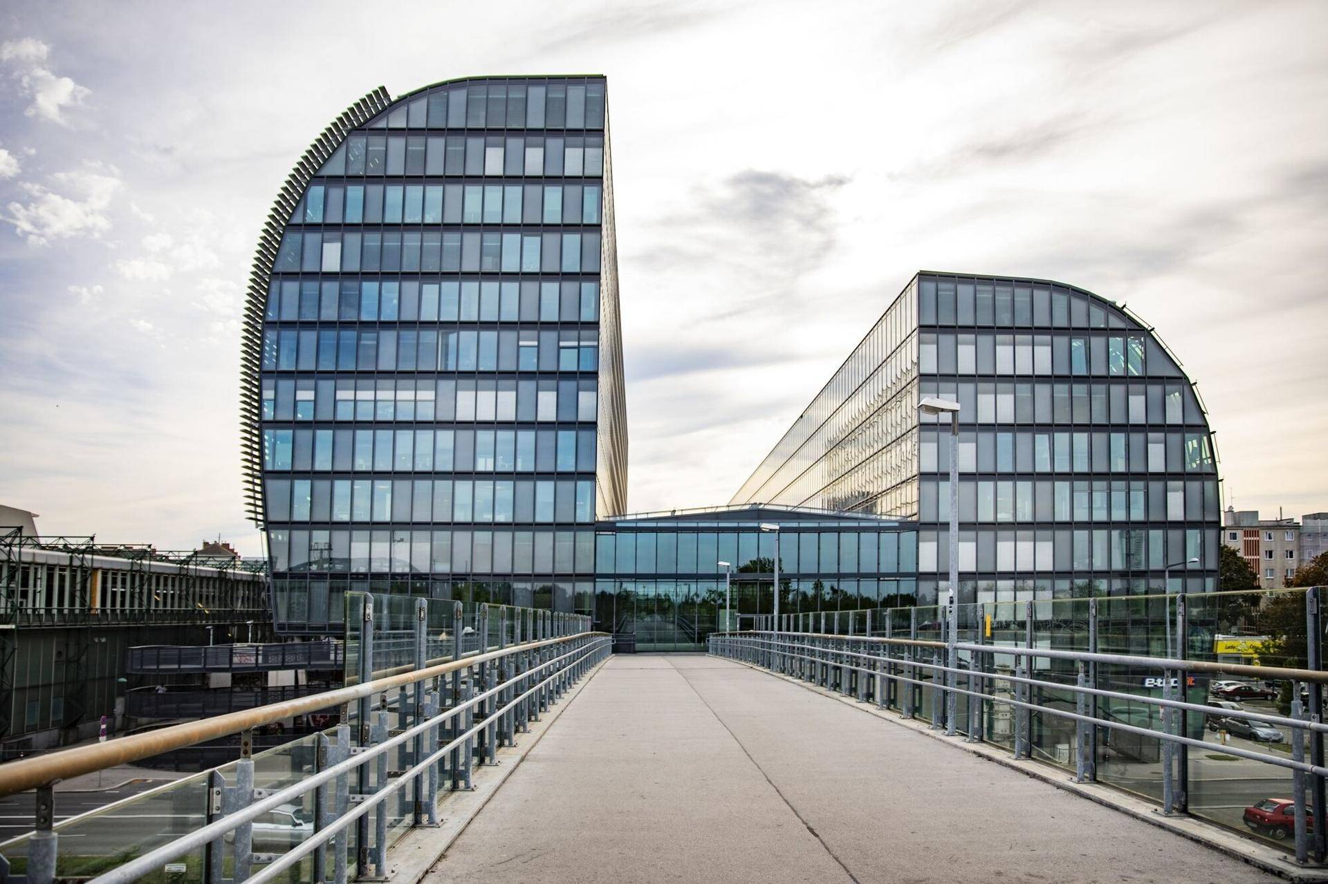 Beeindruckendes Bürogebäude mit geschwungener Glasfassade, verbunden durch eine Brücke, unter einem bewölkten Himmel.