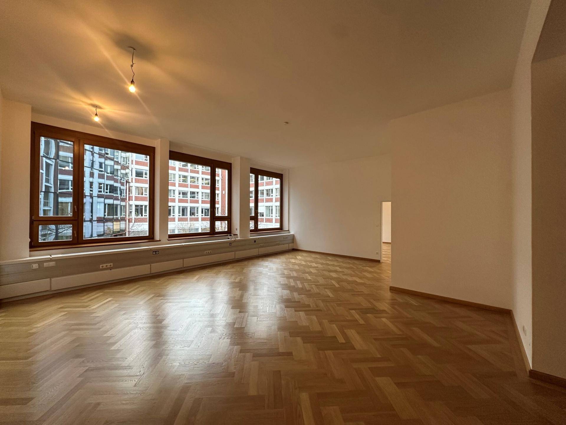Heller Raum mit großen Fenstern und Fischgrätparkett, bietet viel Tageslicht und Stadtblick.