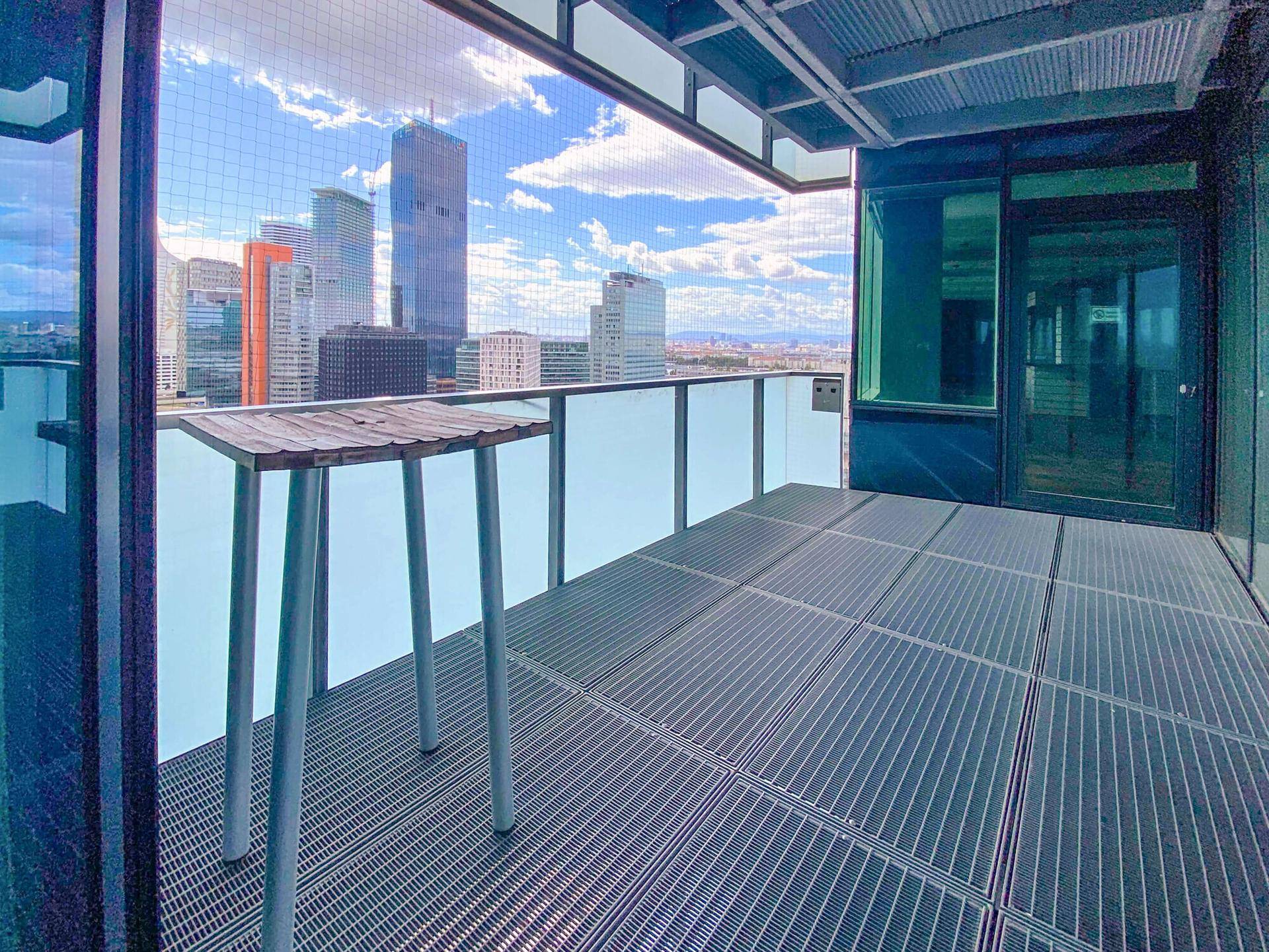 Moderner Balkon mit Metallboden, hohem Tisch und beeindruckendem Stadtpanorama.