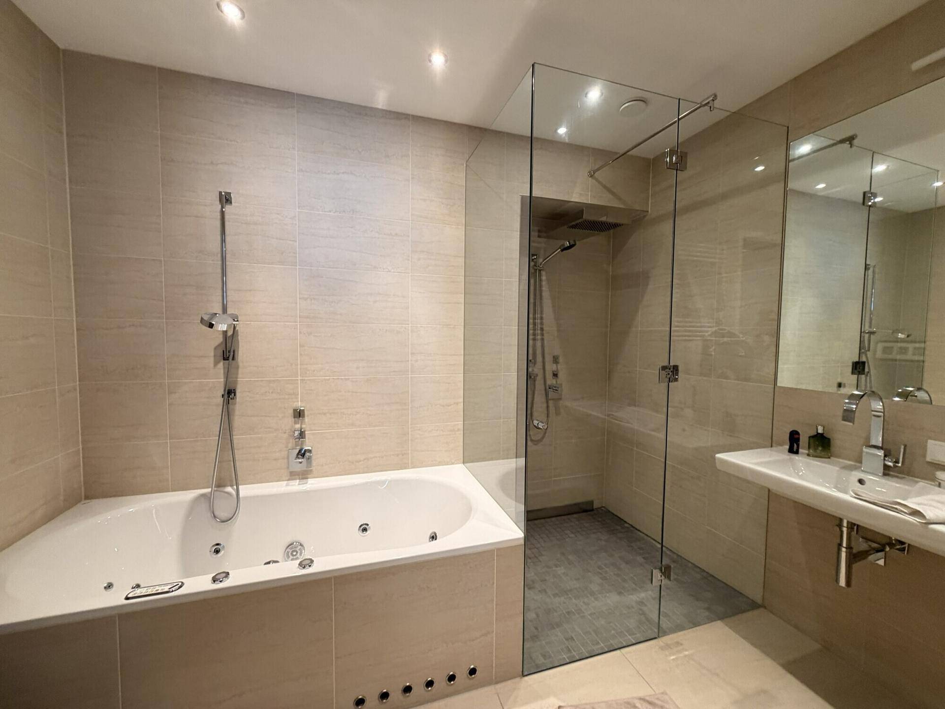 Modernes Badezimmer mit großer Badewanne, begehbarer Dusche und beigefarbenen Fliesen.