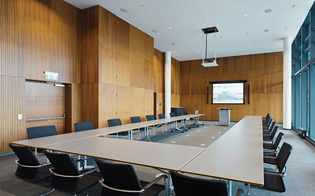 Großer Konferenzraum mit Holzwänden, U-förmiger Tischordnung und einem Beamer für Präsentationen.