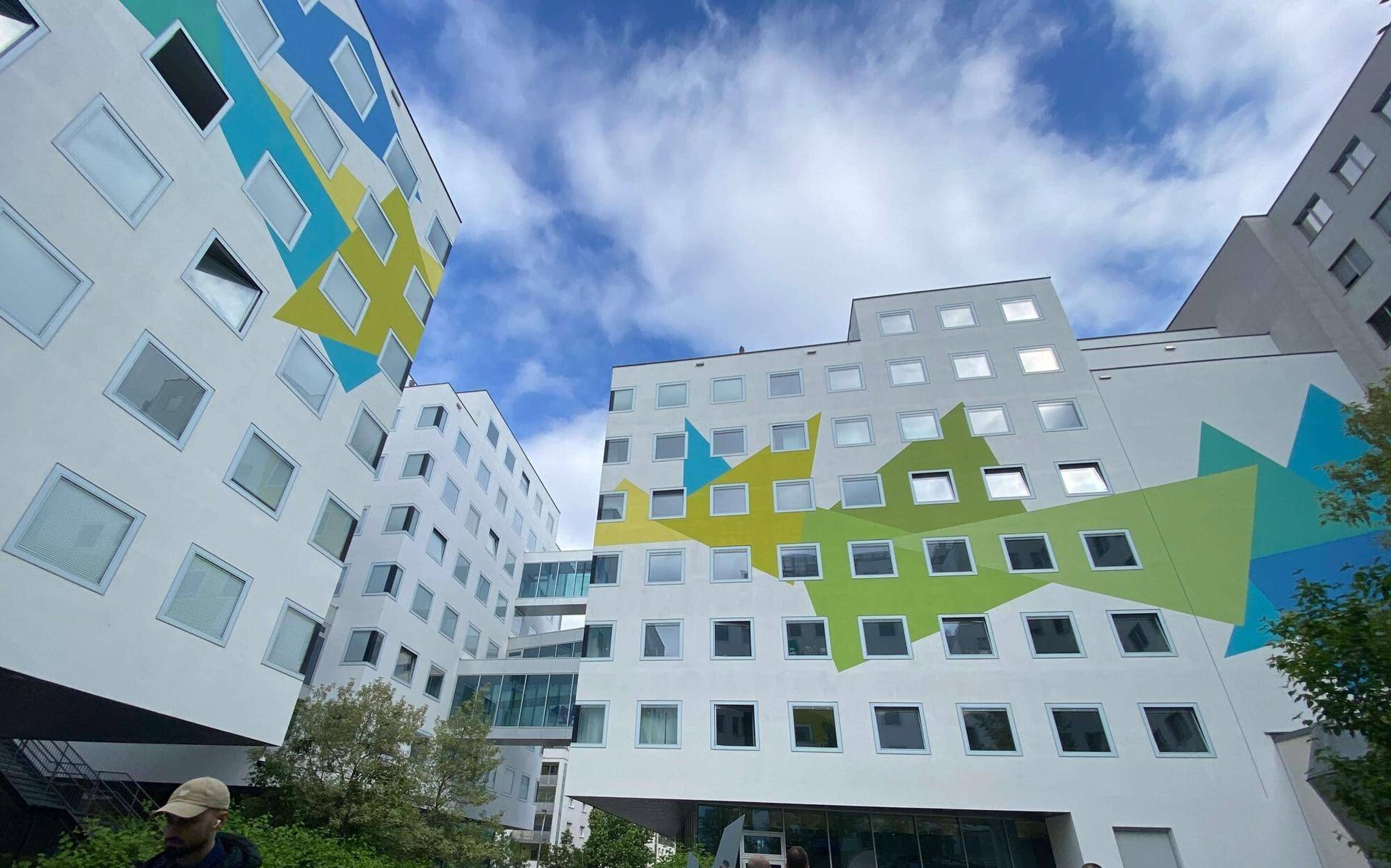 Moderne Gebäudefassaden mit farbenfrohen geometrischen Mustern und gläsernen Verbindungsbrücken unter blauem Himmel.