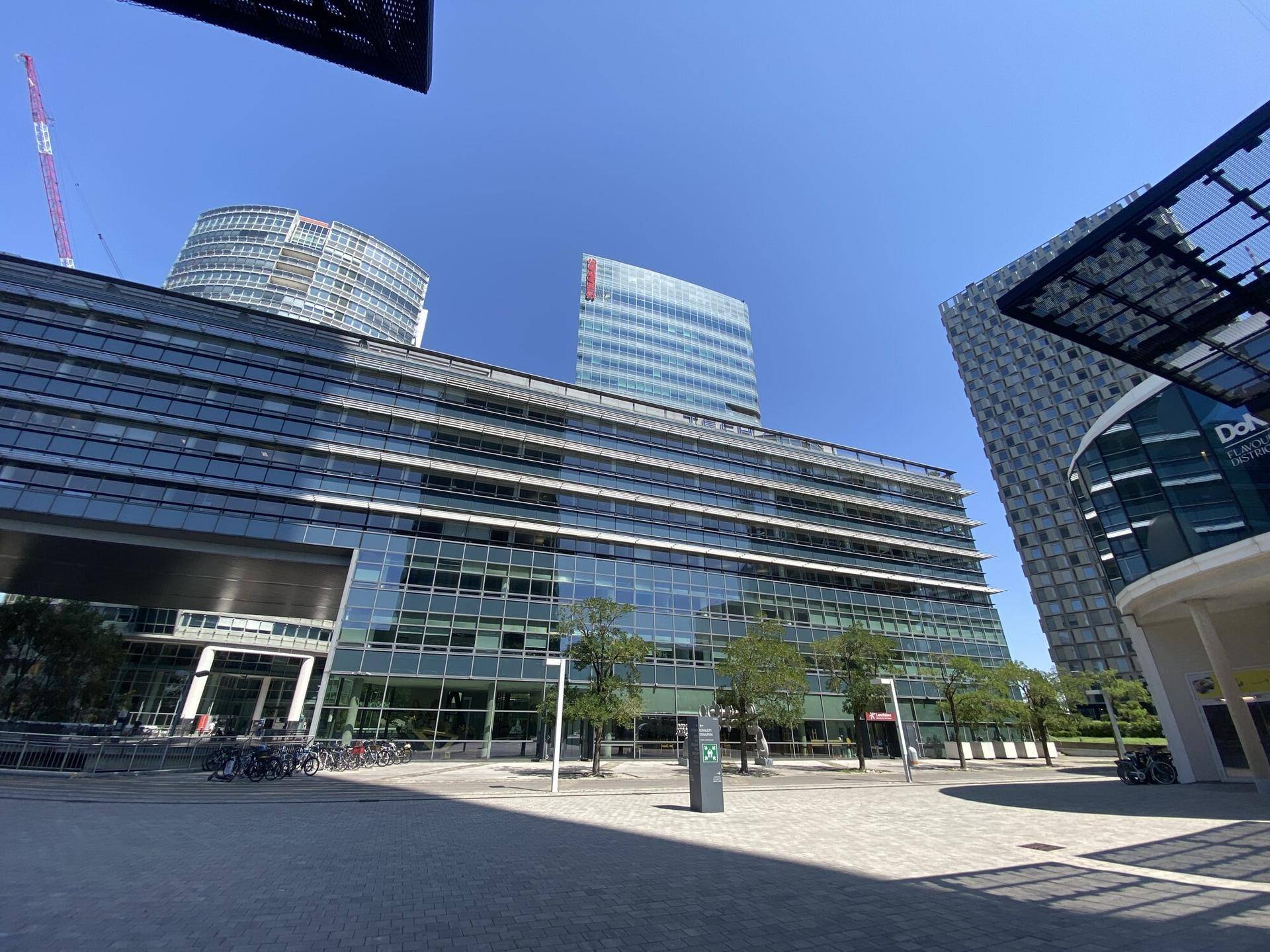 Moderne Bürogebäude mit Glasfassaden und klarem Himmel, umgeben von städtischer Infrastruktur.