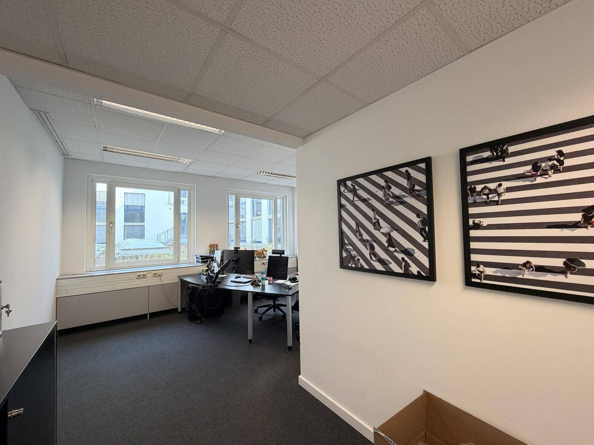 Modernes Büro mit zwei Arbeitsplätzen, großen Fenstern und zeitgenössischer Wandkunst.