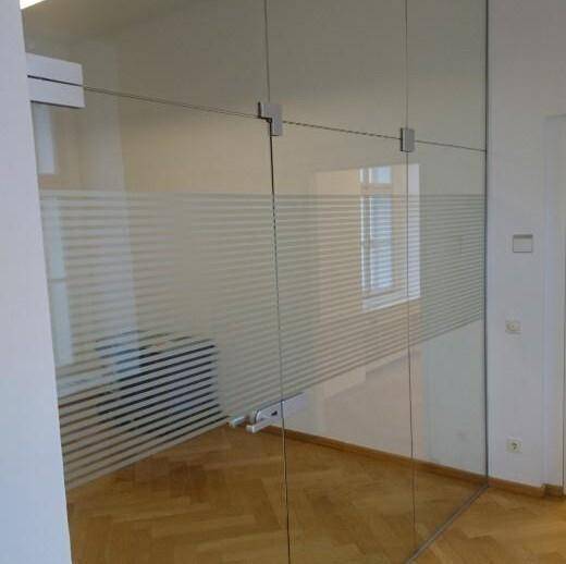 Innenraum mit moderner Glaswand und Milchglasstreifen, die einen Blick auf ein Fenster und Parkettboden freigibt.