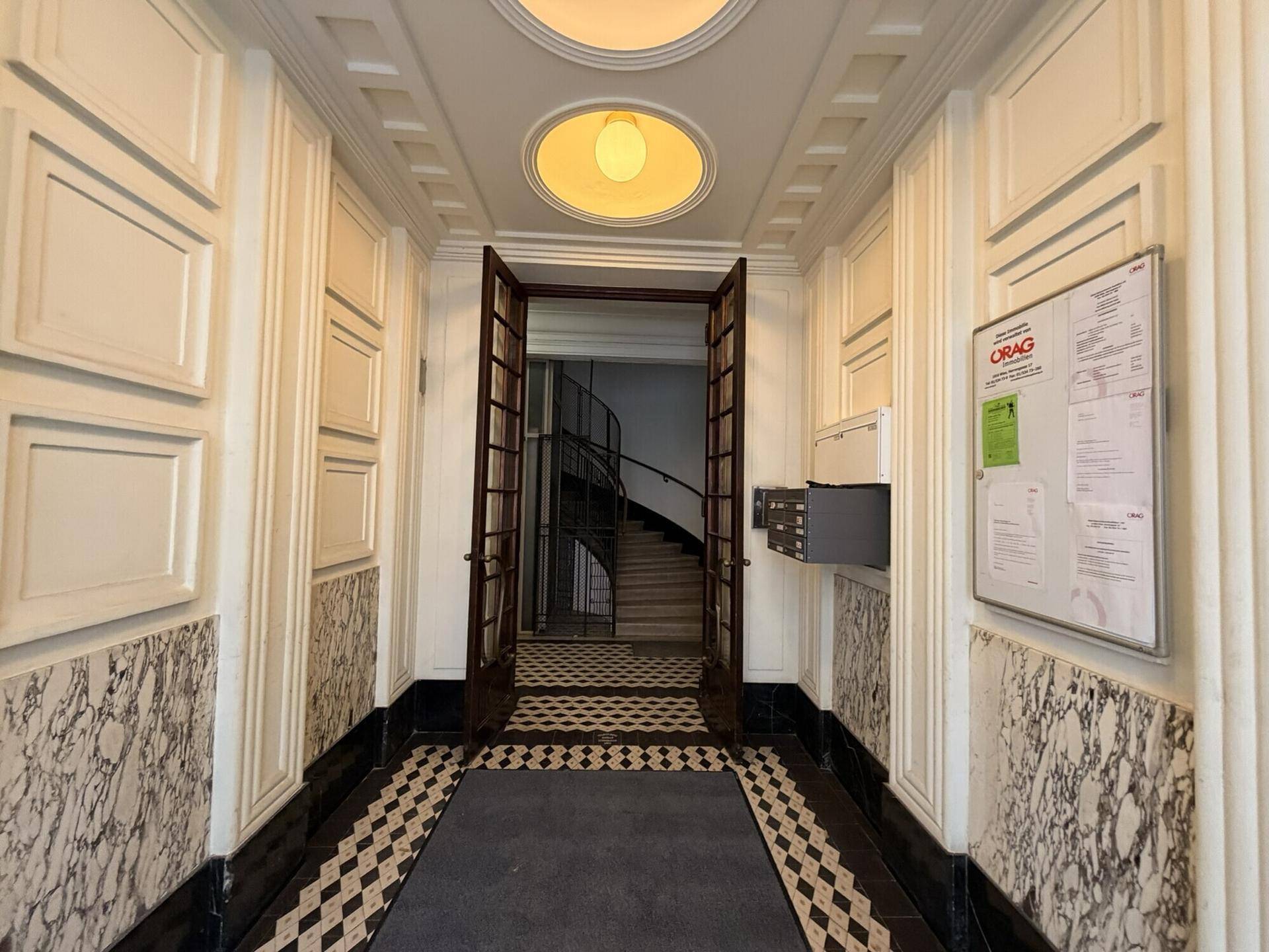 Eleganter Eingangsbereich mit Marmorverkleidung, Schachbrettfliesen und hohen Decken, der zum Treppenhaus führt.