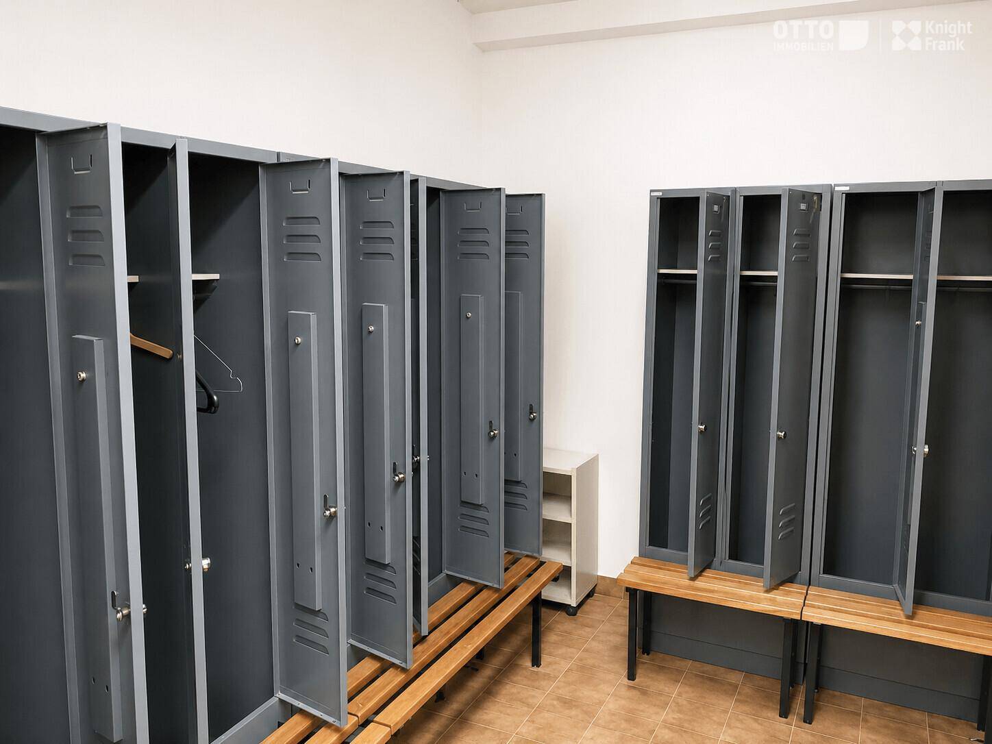 Umkleideraum mit grauen Metallspinden und robusten Holzbänken, ideal für Sport- oder Arbeitsbereiche.