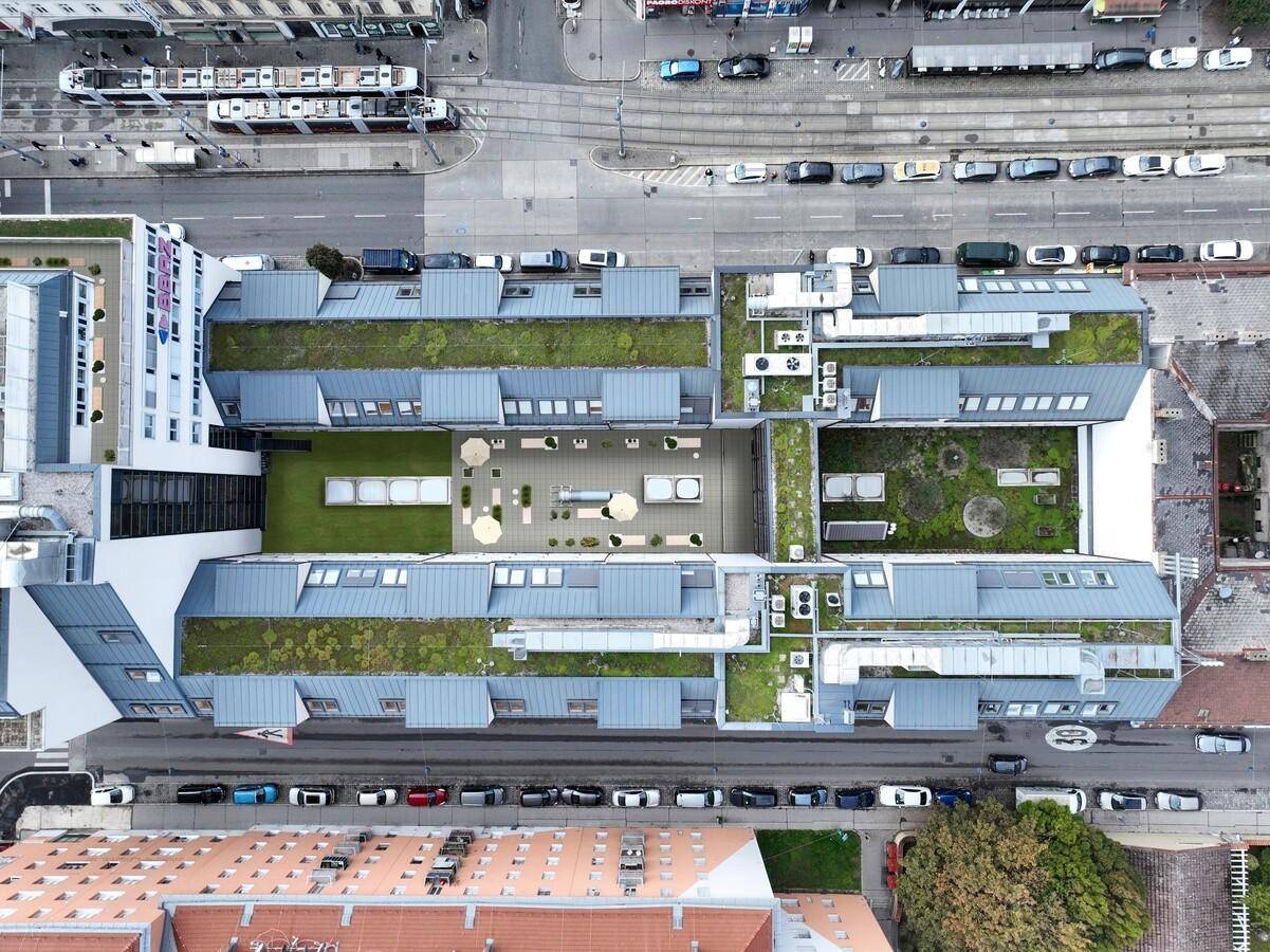 Luftaufnahme eines Gebäudekomplexes mit begrünten Dächern und einem Innenhof mit Sitzgelegenheiten.