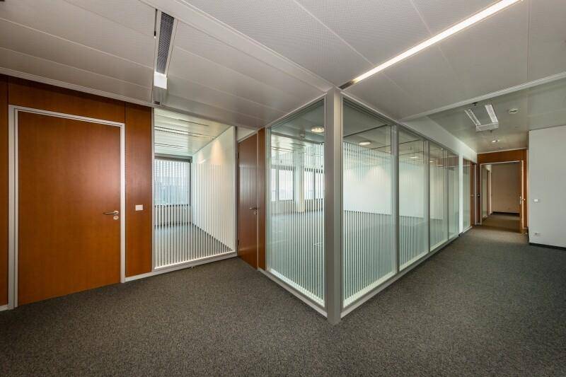 Büroecke mit Teppichboden, modernen Glasbüros und Holztüren, die eine flexible Raumgestaltung ermöglichen.