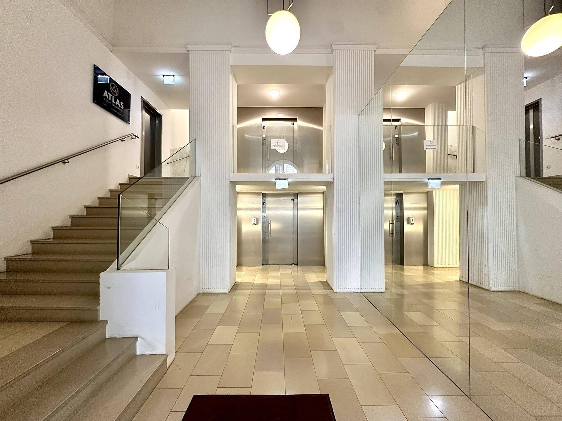 Geräumige Eingangshalle mit Treppenhaus, mehreren Aufzügen und modernen Spiegelflächen.