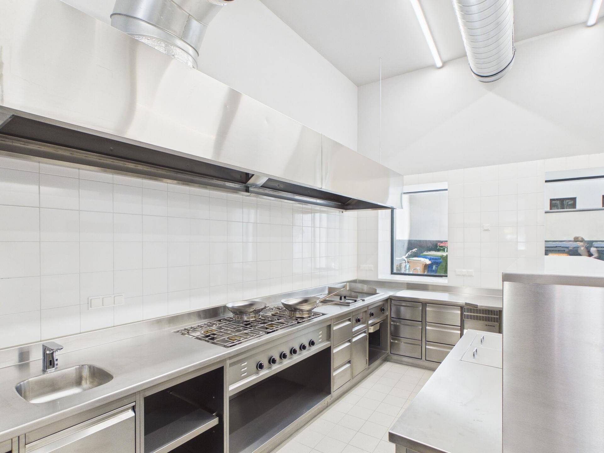 Professionelle Großküche mit Edelstahlgeräten, Fliesenwänden und Abluftsystem für den Gastronomiebetrieb.