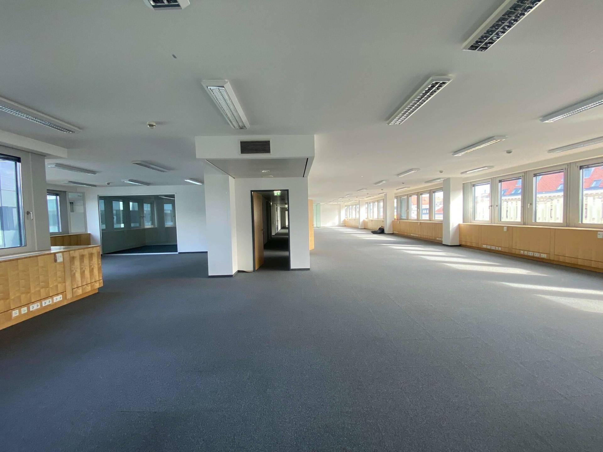 Großes, offenes Büro mit Teppichboden und vielen Fenstern, die viel Tageslicht bieten.
