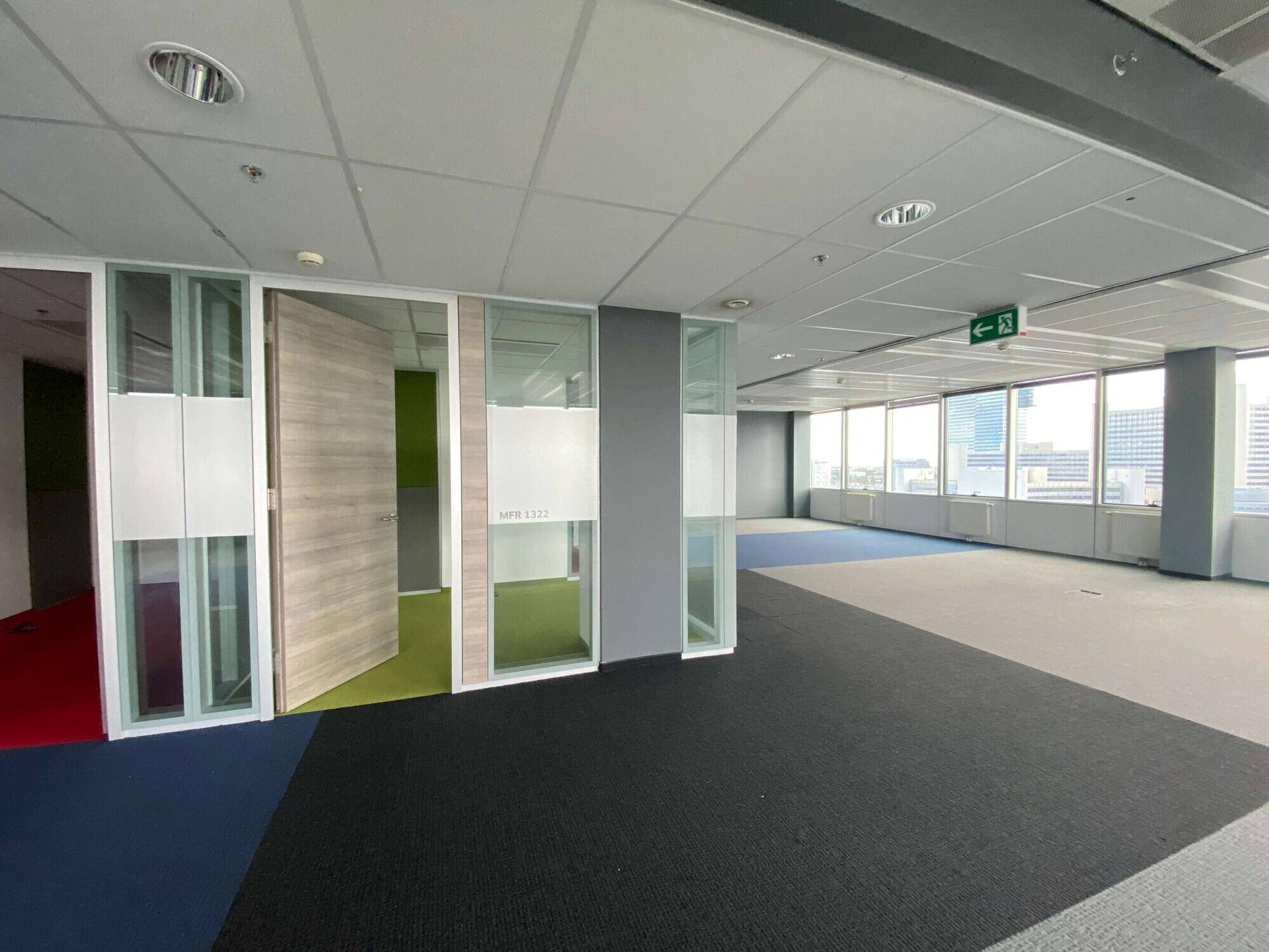 Moderner Bürobereich mit Glaswänden, Teppichboden und einem Ausgangsschild, der verschiedene Arbeitsbereiche zeigt.