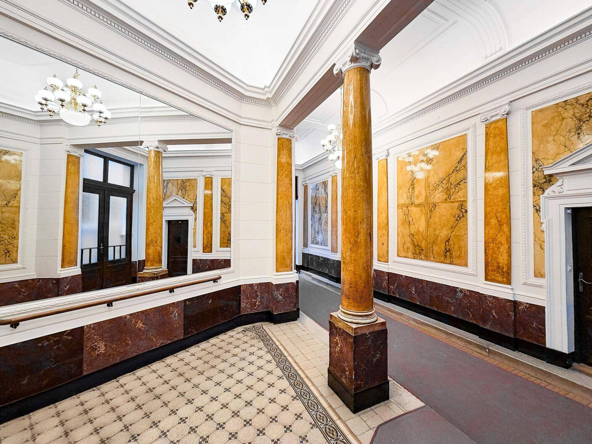 Prunkvolle Eingangshalle mit Marmorverkleidung, Säulen, gemustertem Fliesenboden und eleganten Kronleuchtern, die den historischen Stil betont.