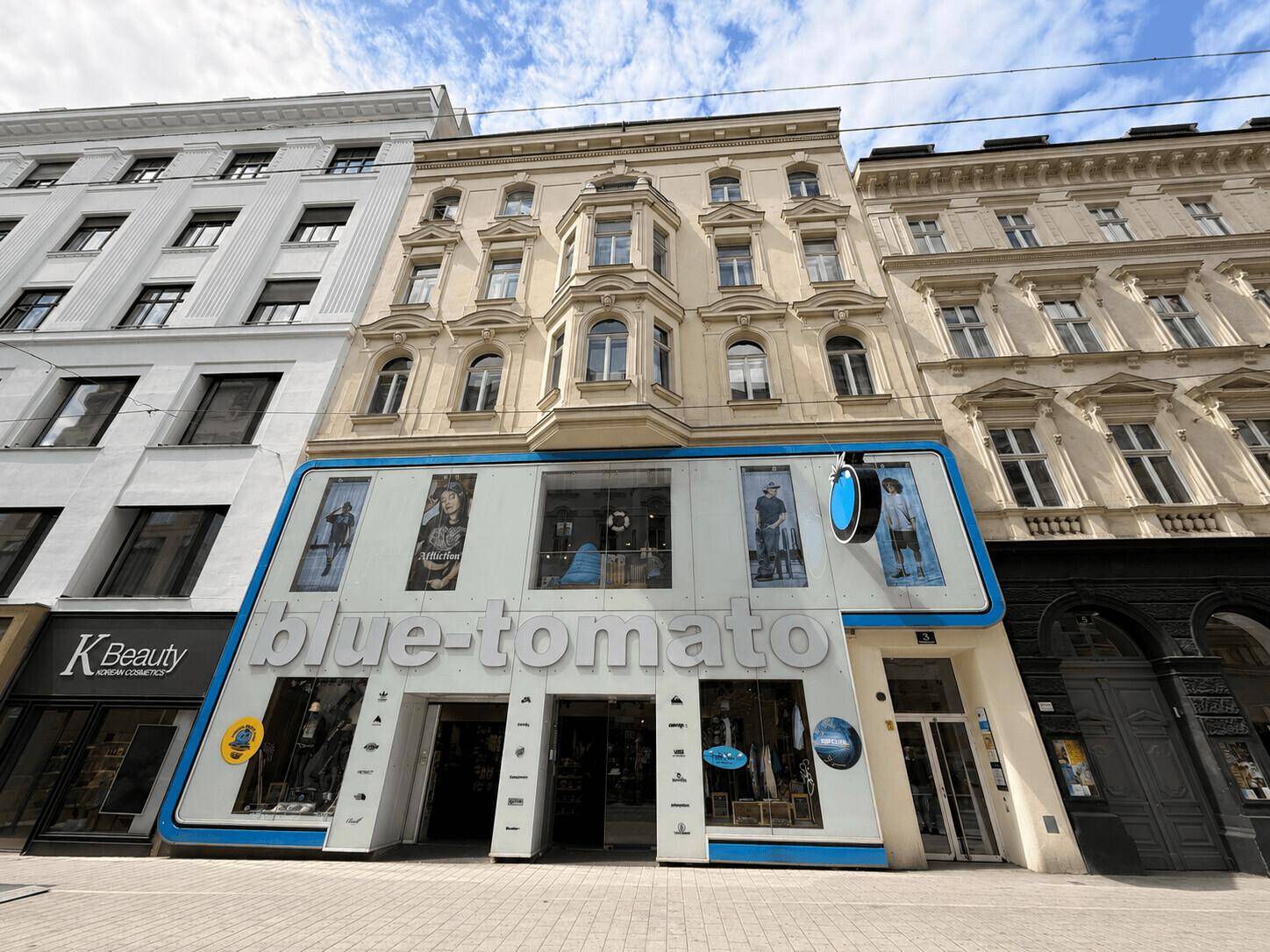 Historisches Gebäude mit moderner Ladenfront und großen Schaufenstern in einer belebten Straße.