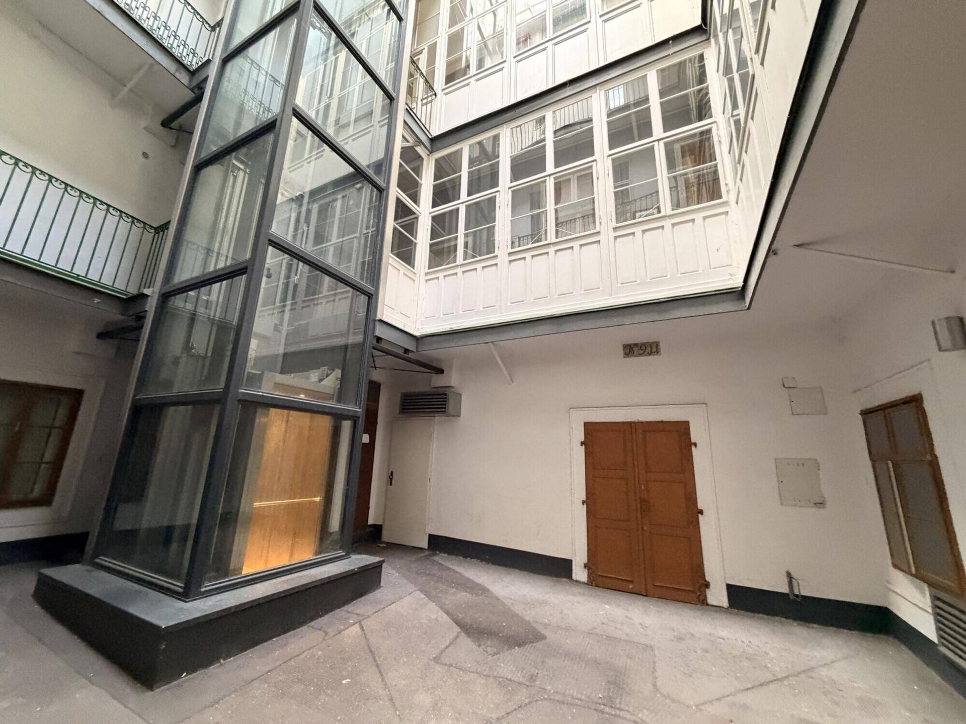 Innenhof mit modernem Glasaufzug und traditionellen Fensterfronten, der eine einzigartige Mischung bietet.