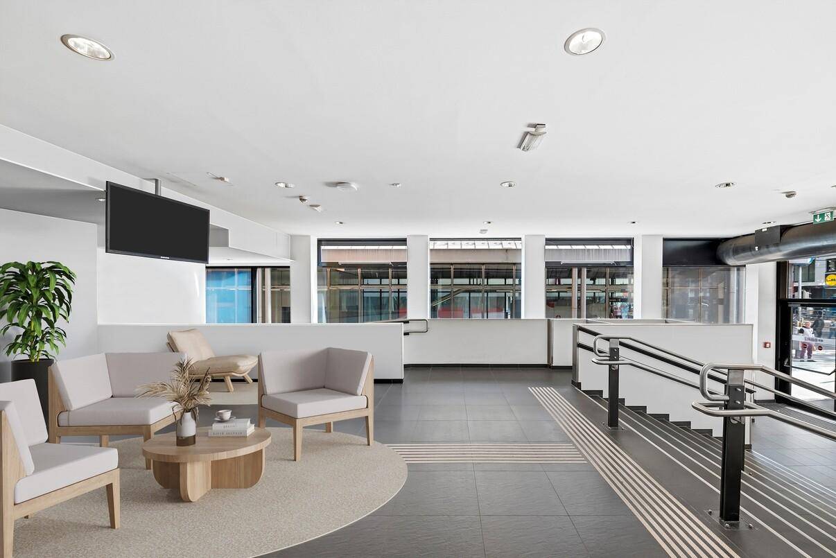 Moderne Lobby mit Sitzgelegenheiten, dunklen Fliesen und Treppenaufgang mit Handlauf.